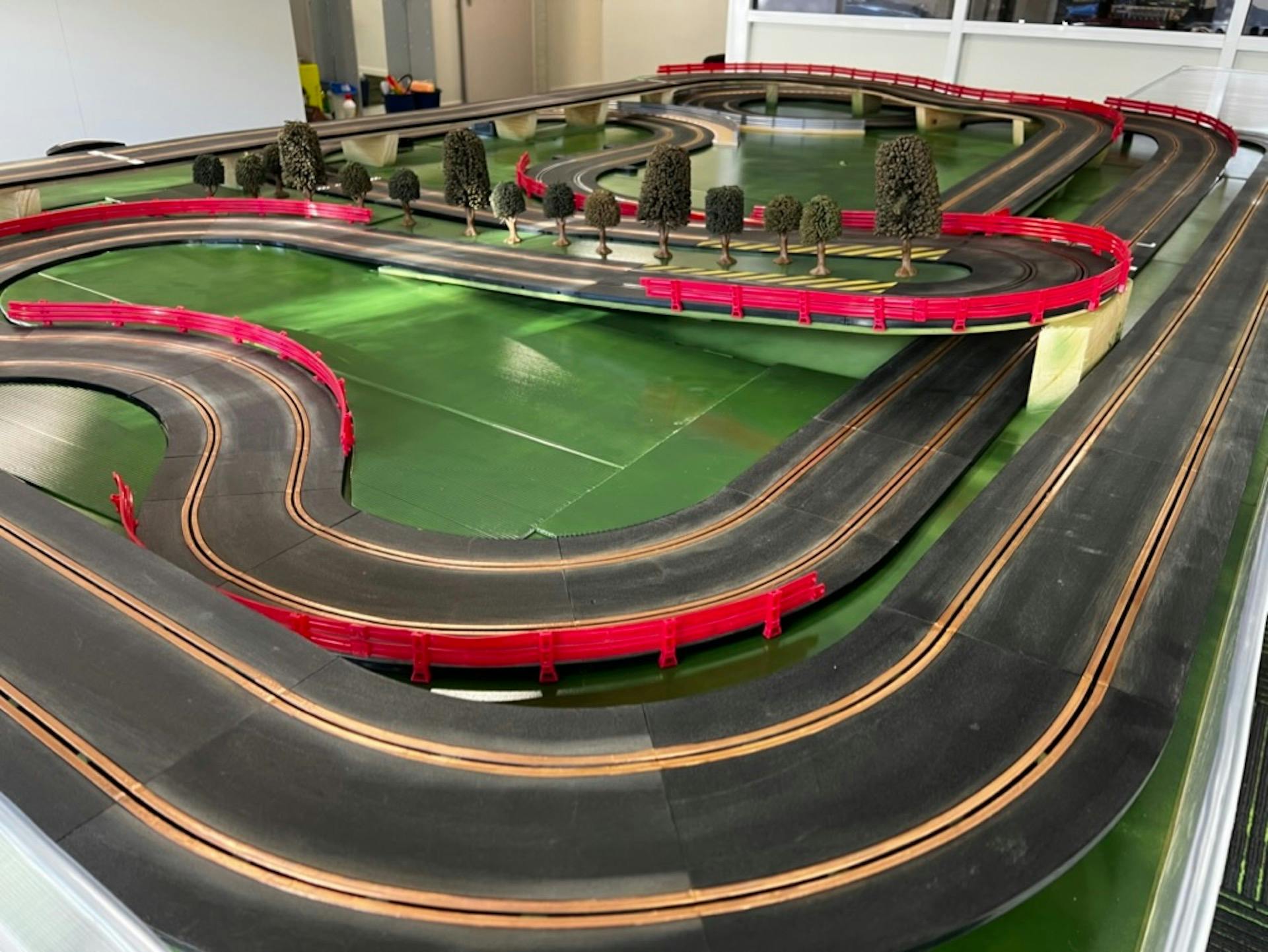 A winding slot car track with red barriers and miniature trees.