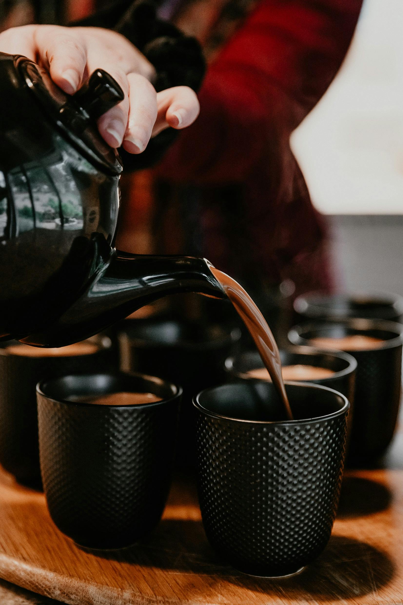 A woman pours ceremonial cacao from a black teapot into black cups.