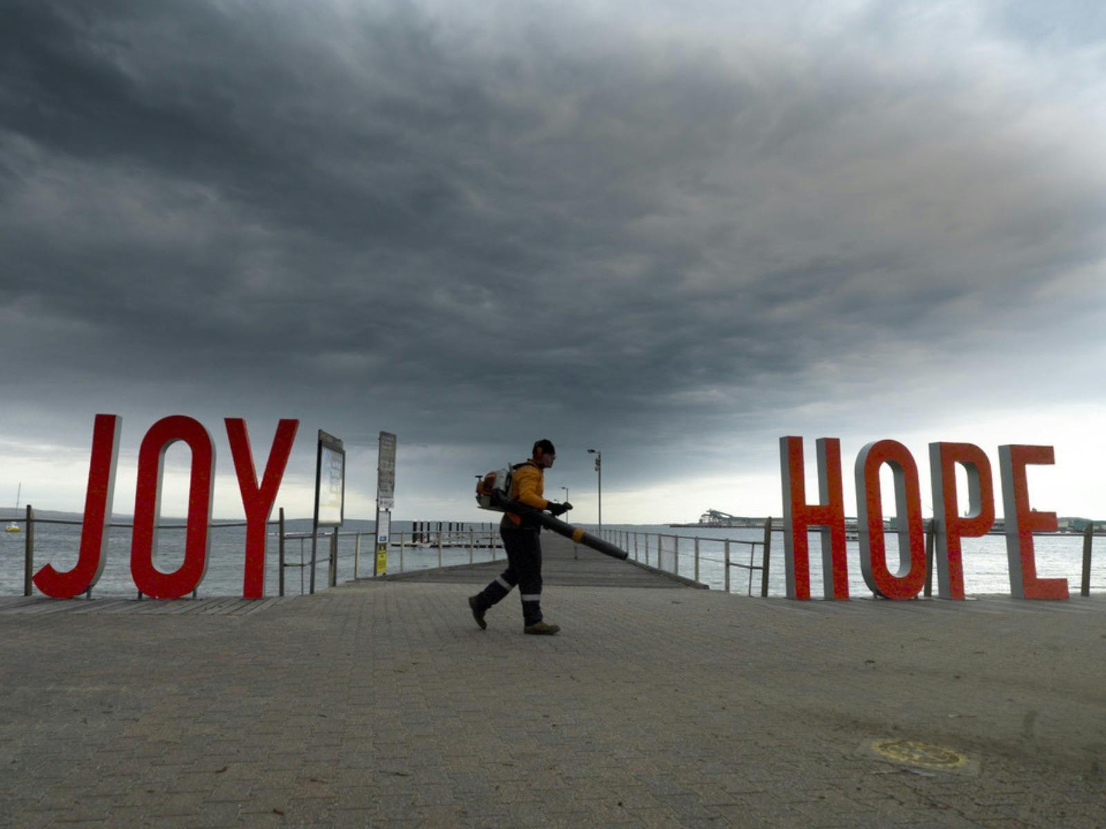 Red large words saying joy and hope on a beach front with a man walking in between