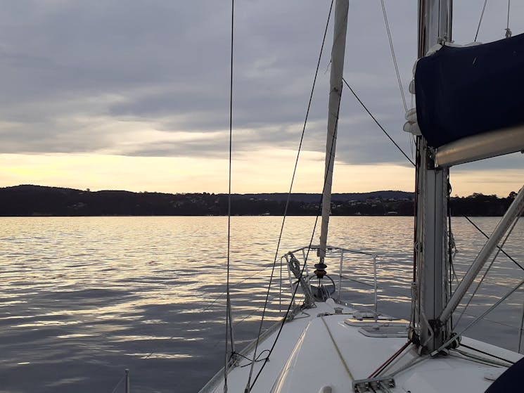 Luxury sailing boat sailing along smooth waters at sunset towards land