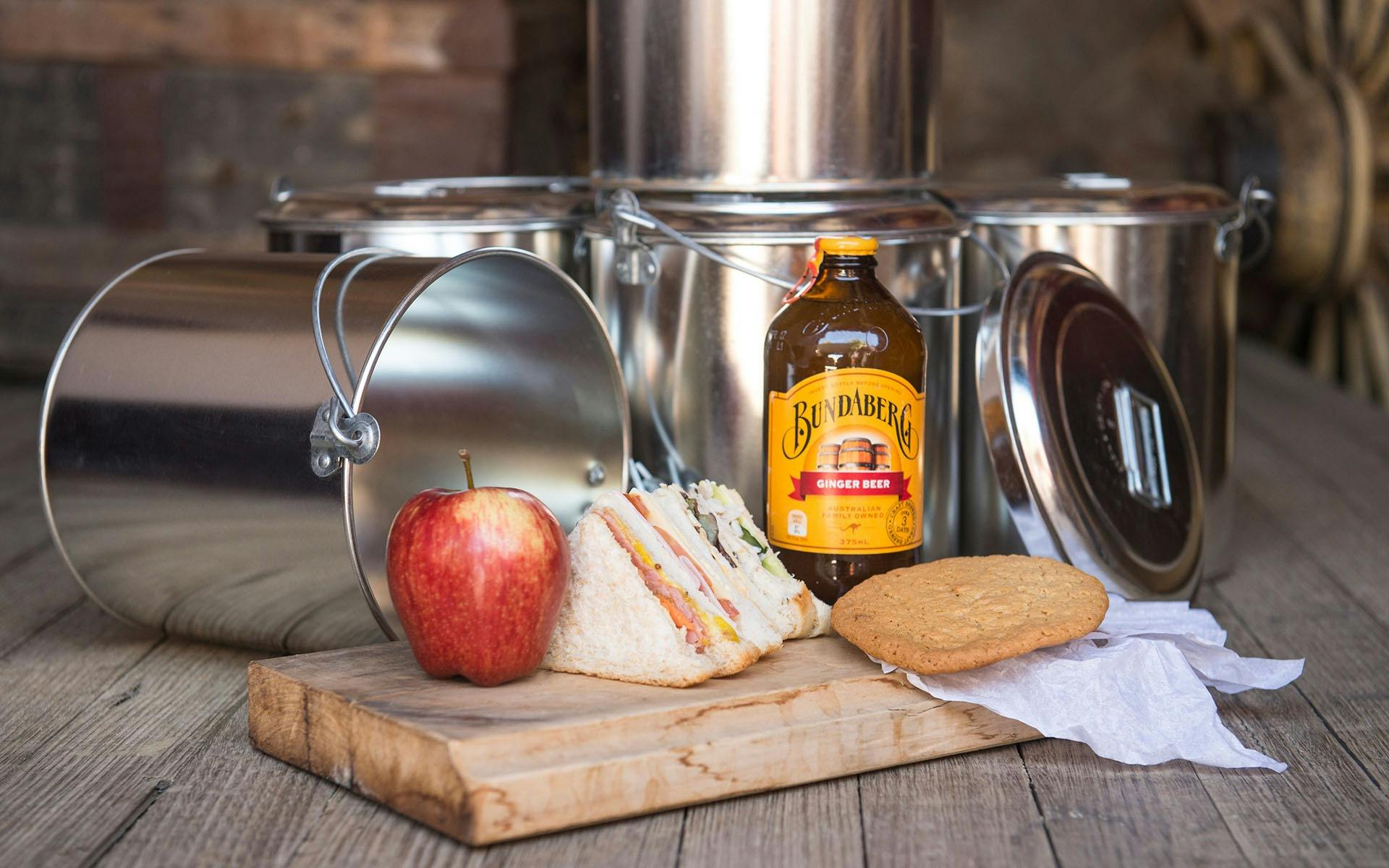 A billy-can lunch including  a cut sandwich, anzac biscuit, apple, and ginger beer