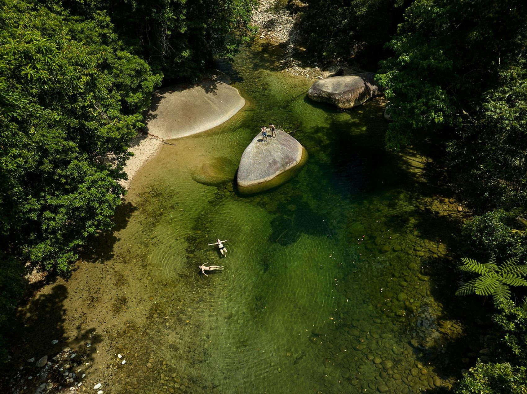 Aerial view of guest swimming in the water hole surrounded by lush rainforest at Babinda Boulders