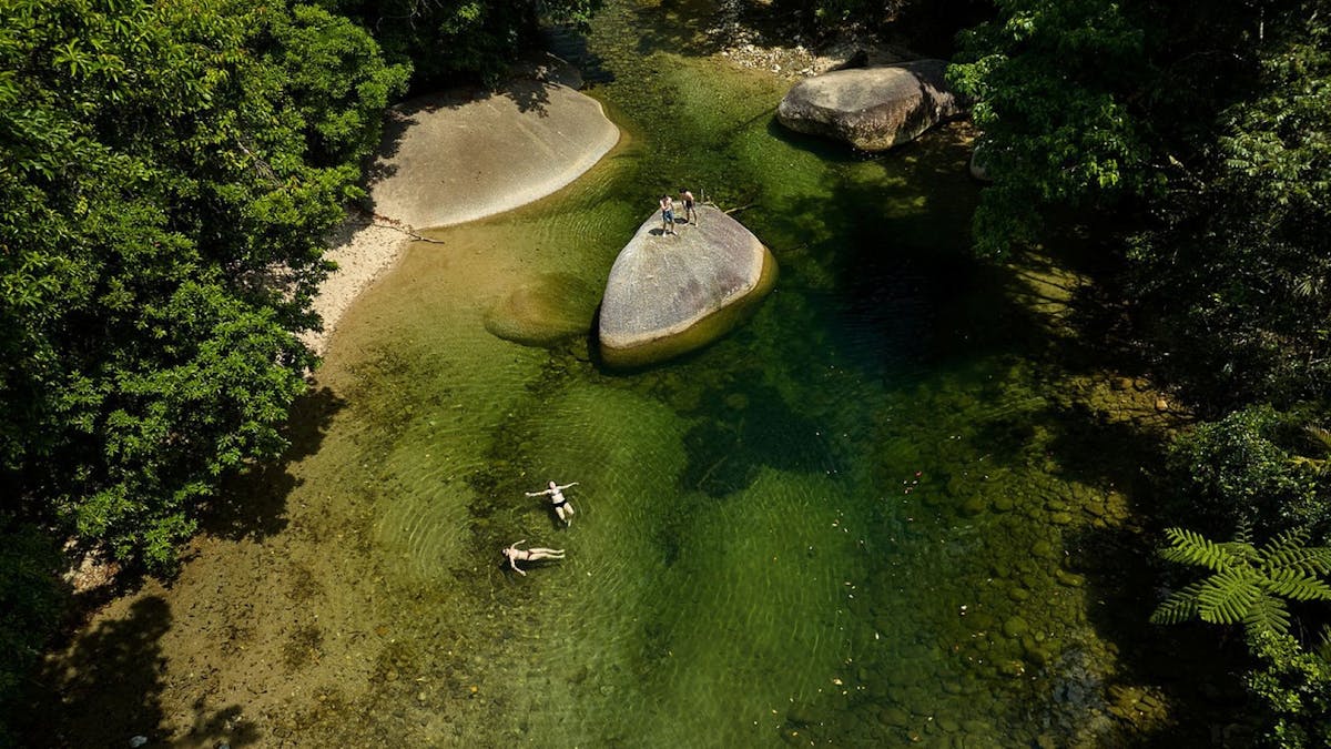 Aerial view of guest swimming in the water hole surrounded by lush rainforest at Babinda Boulders