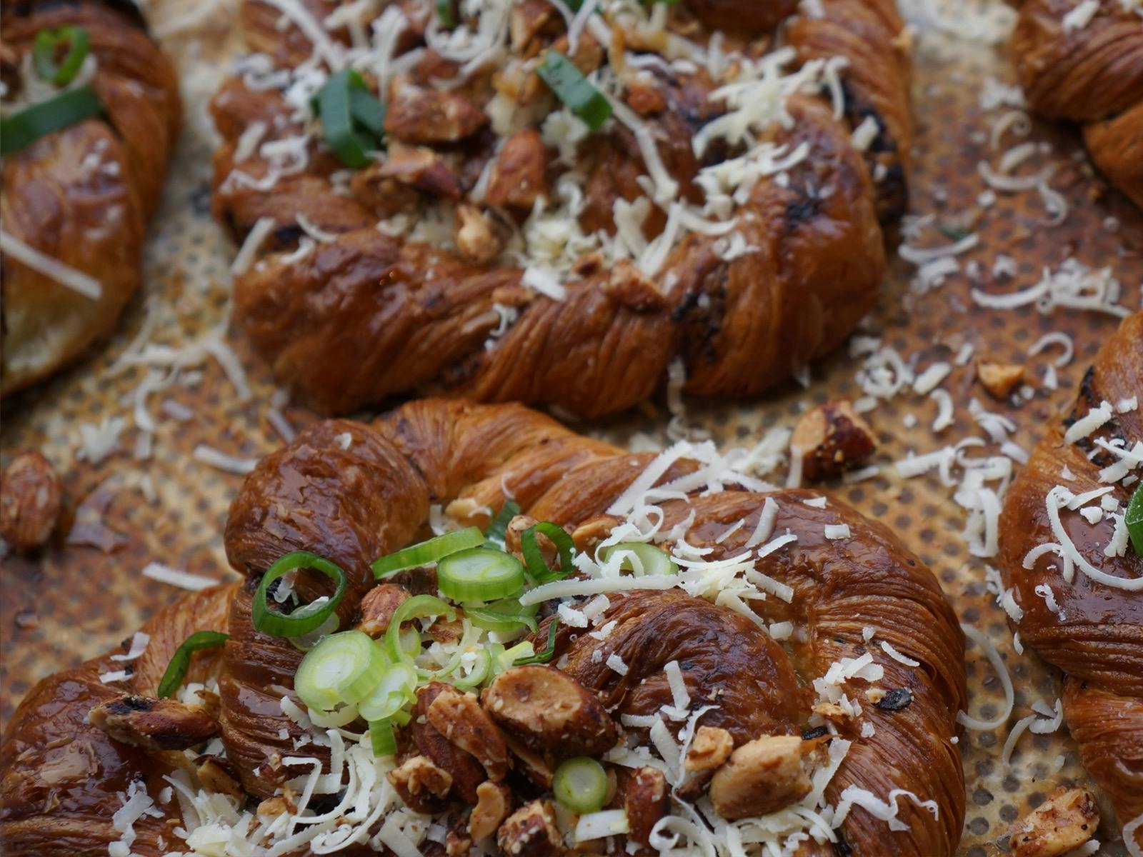 Savoury Twist croissant dough on a baking tray finished with cheddar cheese and fresh cut shallots