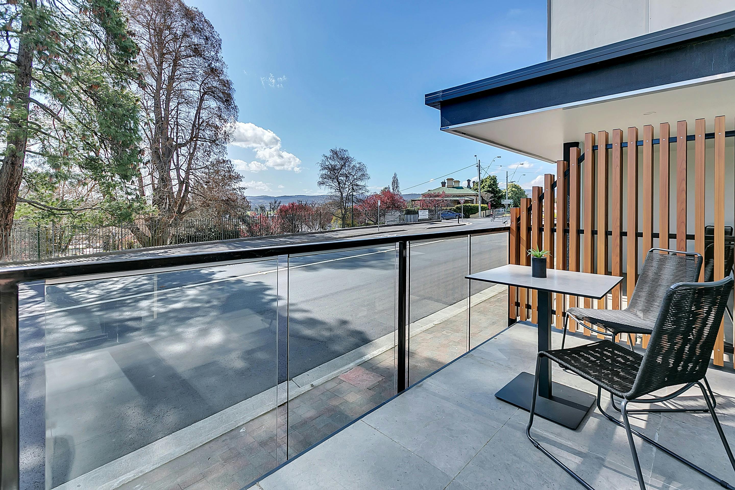 Accommodation room balcony, with view across street to park with large trees.