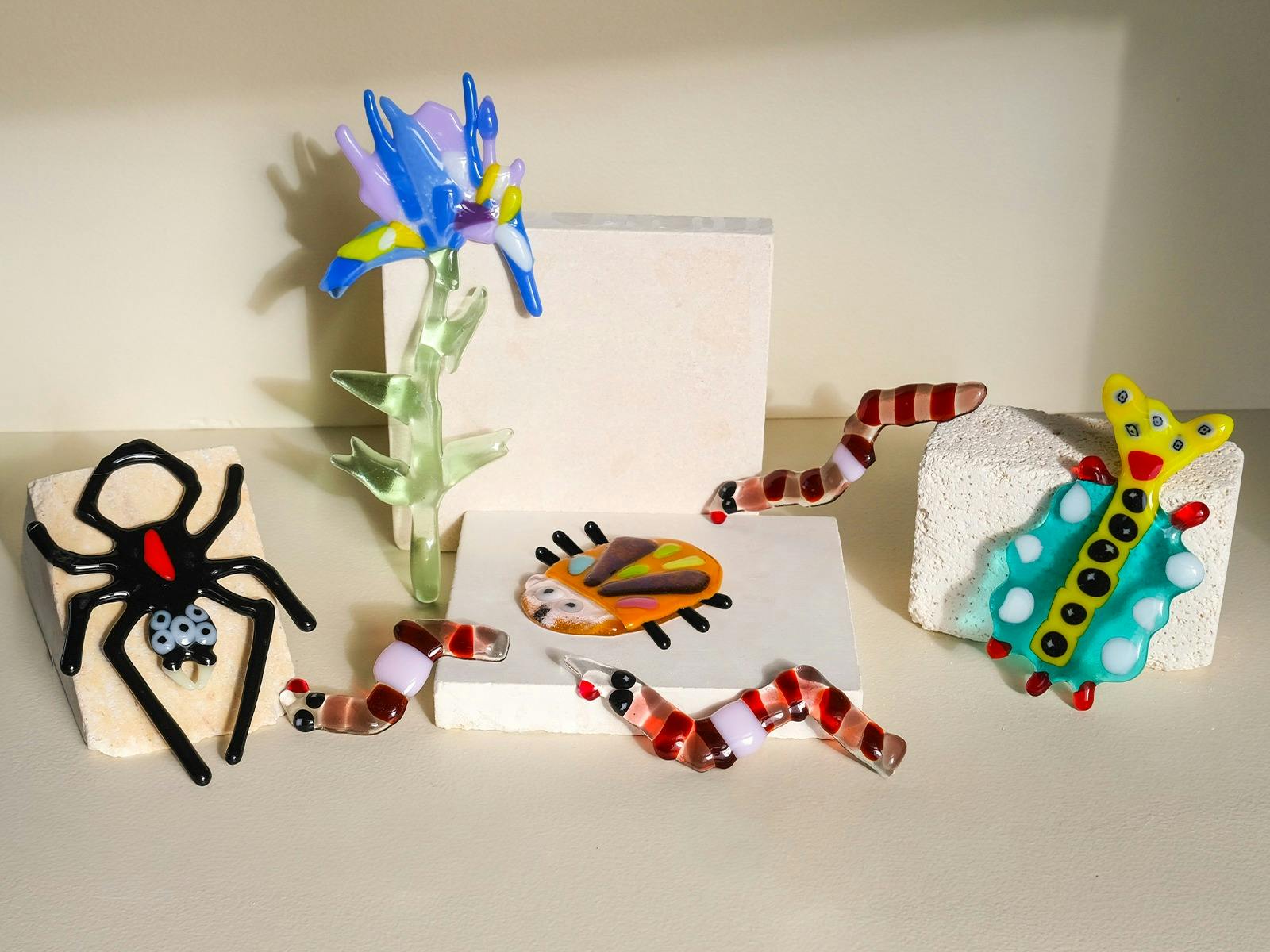 Colorful glass flowers, bugs and worms climbing over kiln blocks, surrounded by glass shards and too