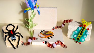 Colorful glass flowers, bugs and worms climbing over kiln blocks, surrounded by glass shards and too