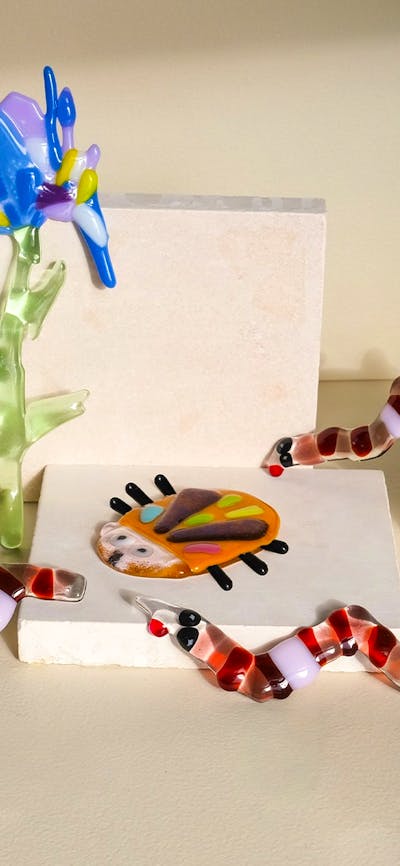 Colorful glass flowers, bugs and worms climbing over kiln blocks, surrounded by glass shards and too