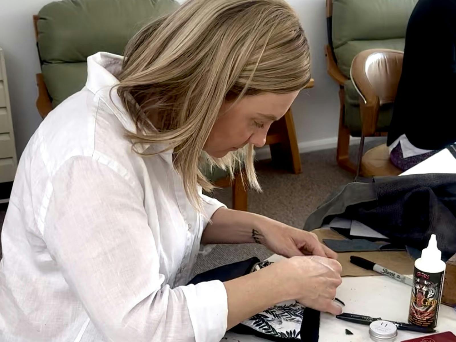 Woman focused on crafting a leather item at a workshop table with tools and materials around her