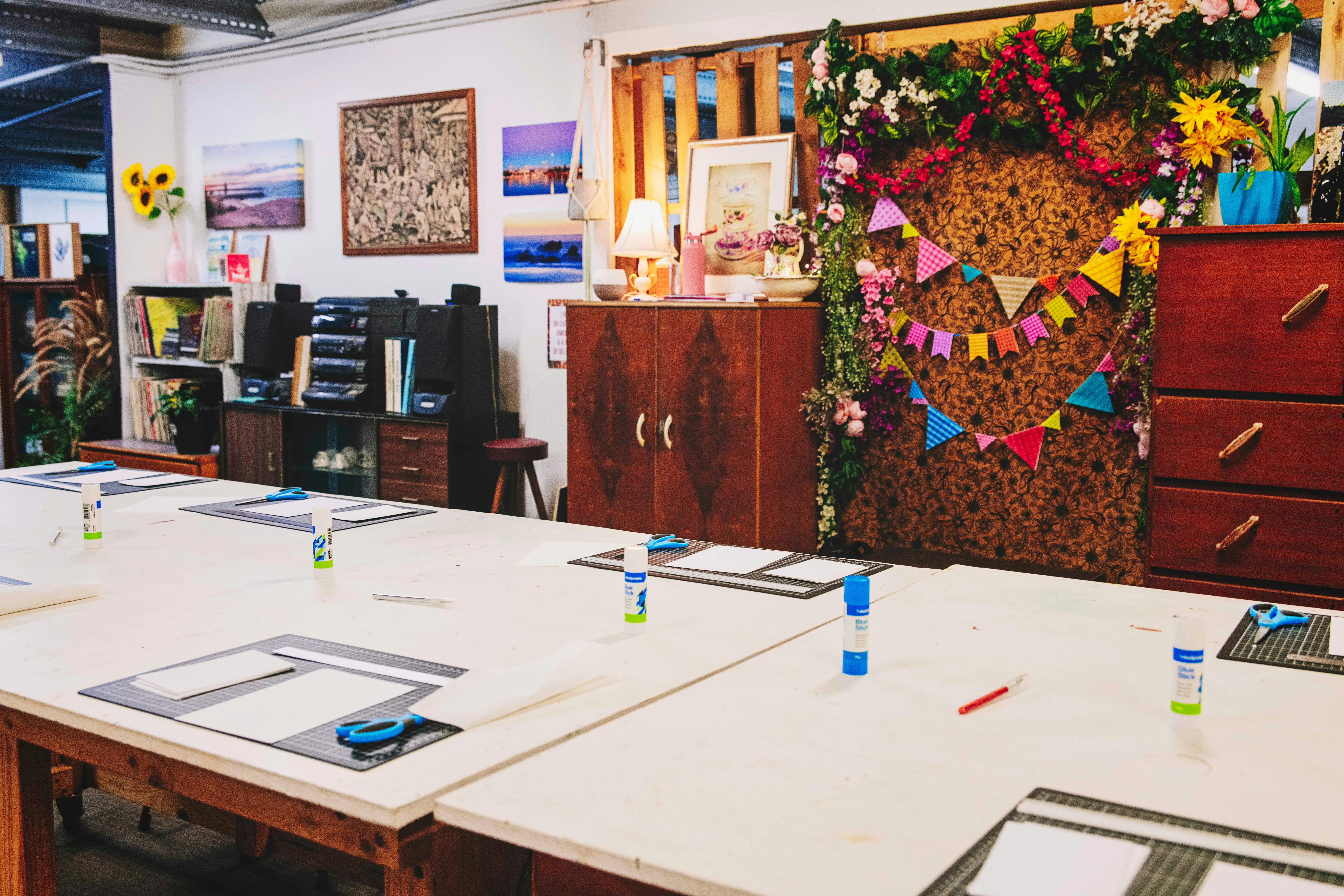 Für eine kreative Session aufgestellte Tische, dahinter farbenfrohe Raumdekorationen an der Wand.