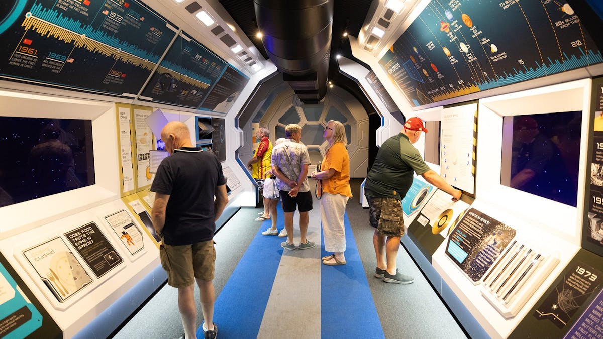 Guests walking through the Cosmos Shuttle inside the interactive exhibit, reading and interacting