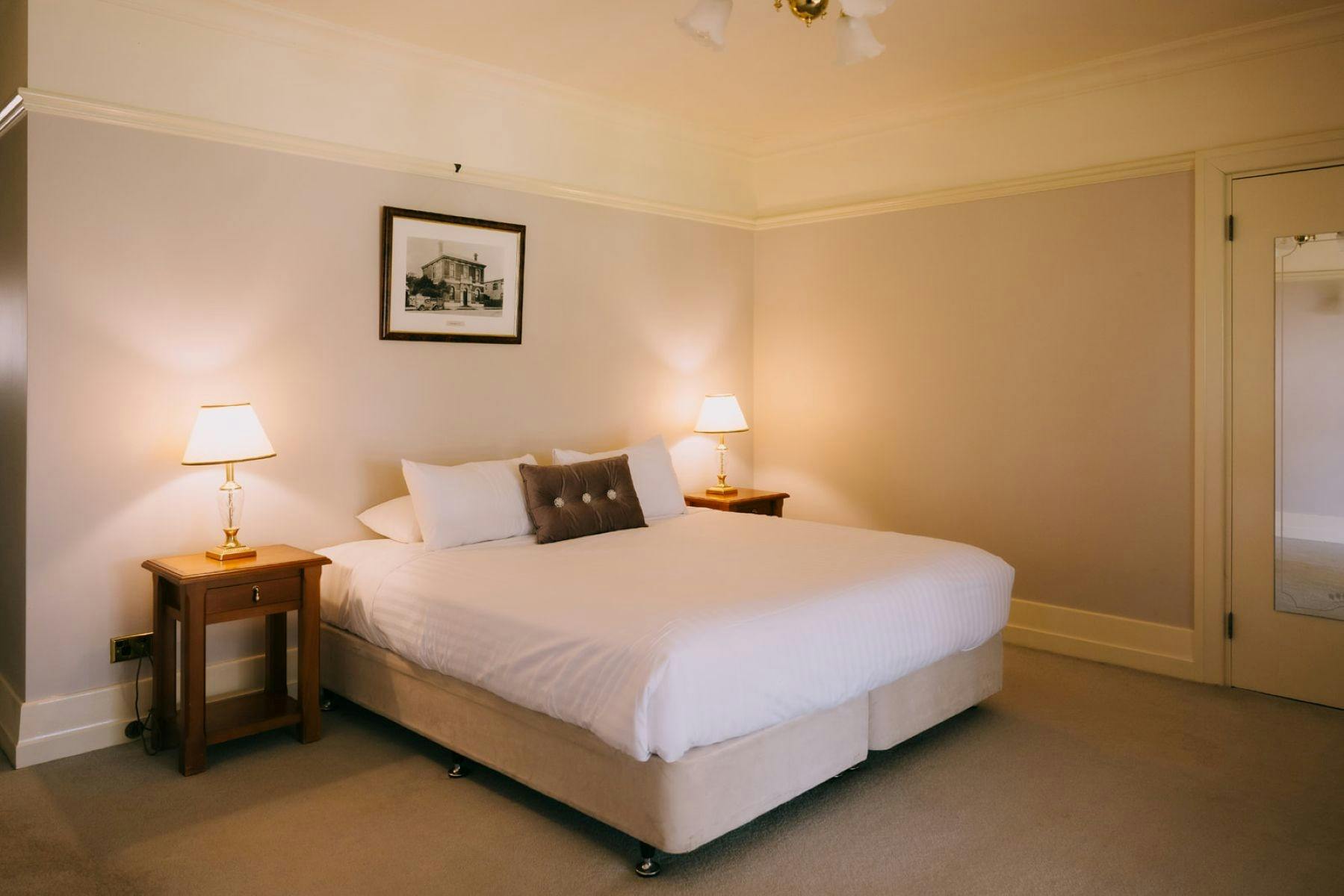 A spacious hotel room with a large bed, two nightstands with lamps, and framed artwork on the wall.