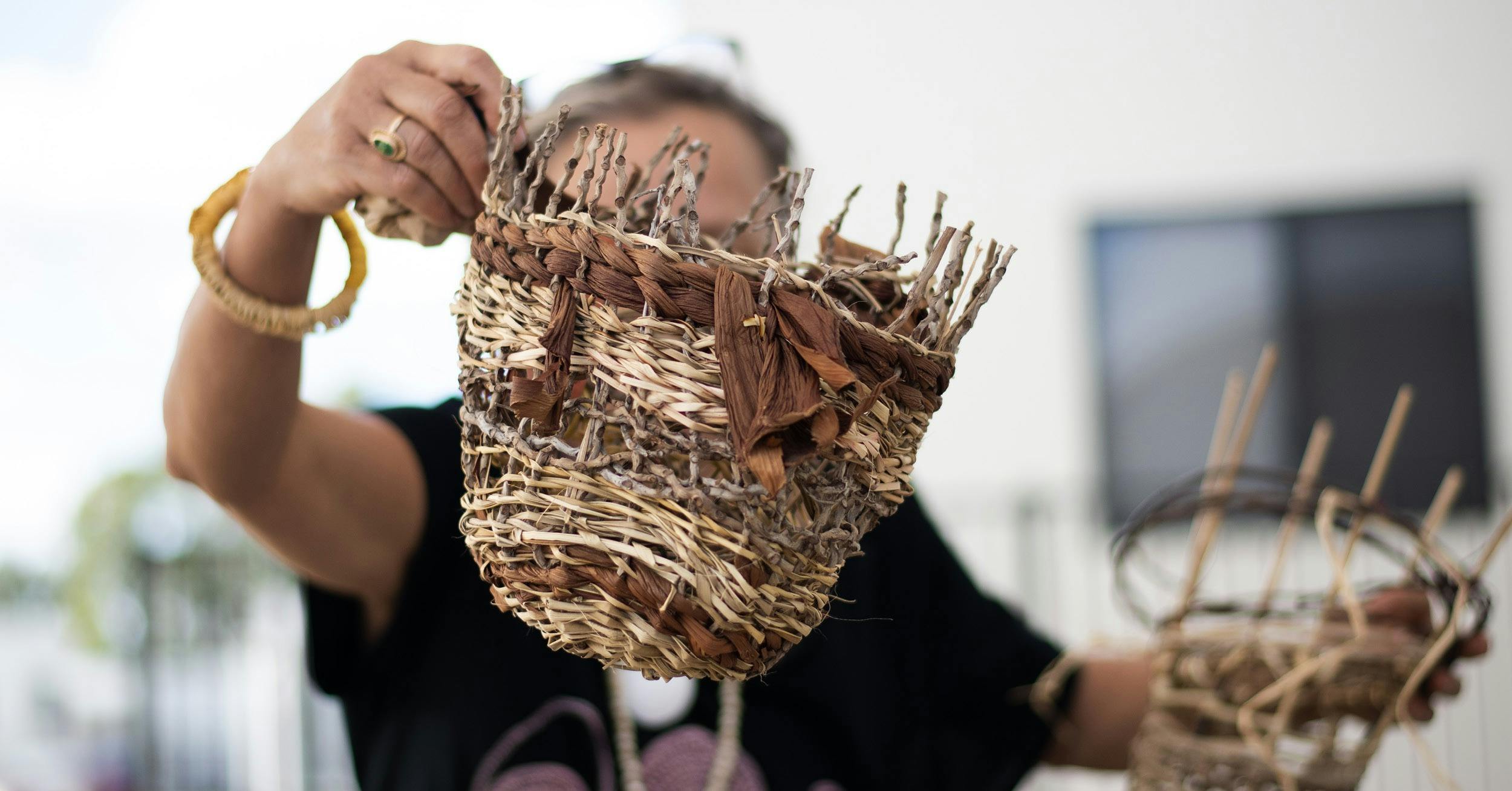 Weaver holds up a random weave basket made from natural materials in front of her face.
