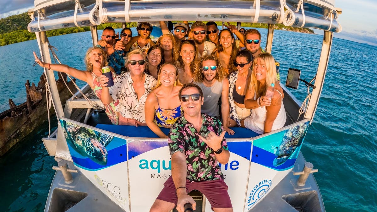 front of boat with large group of people taking a birthday selfie laughing, late afternoon  sunset