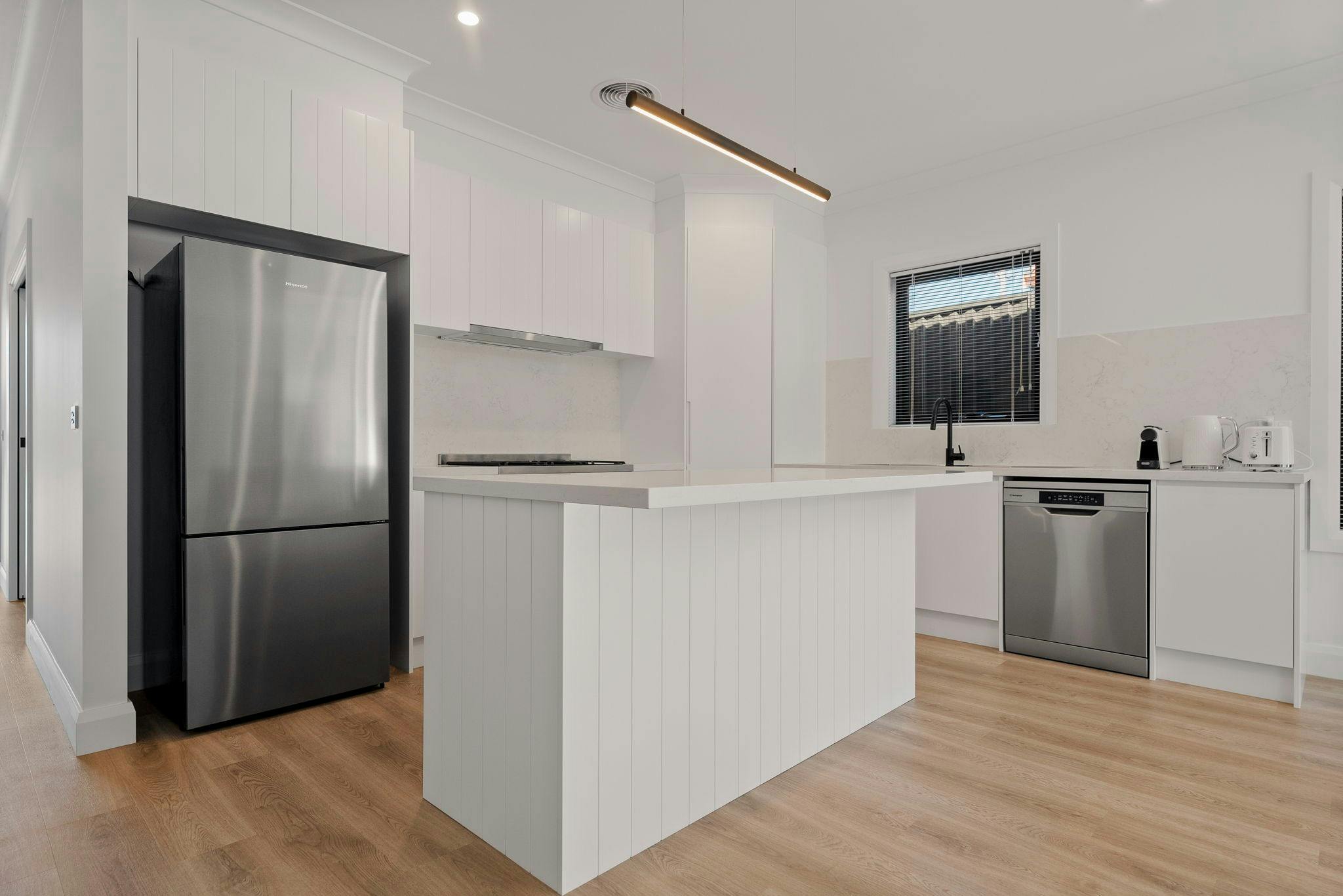 Kitchen with white cabinets, white benchtops, island bench, wooden floors, chrome appliances