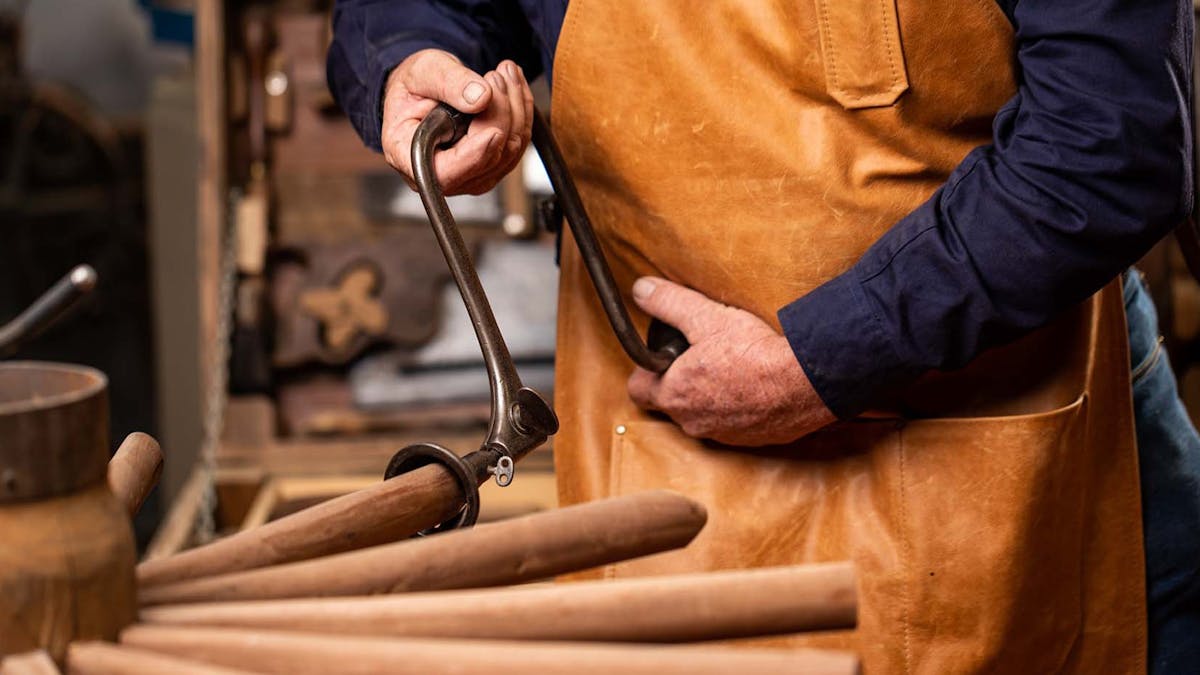 Man working on wooden wheel spokes with tool.