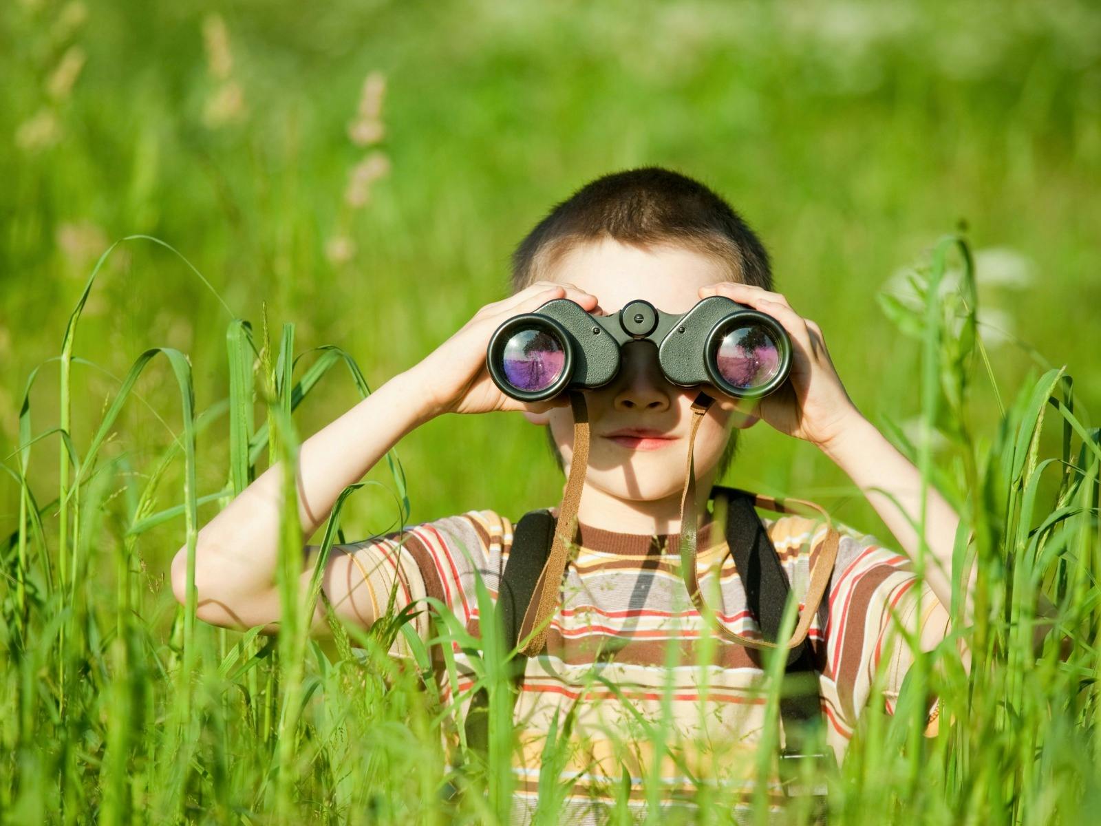 Young boy holds binoculars up as he stands in tall grass