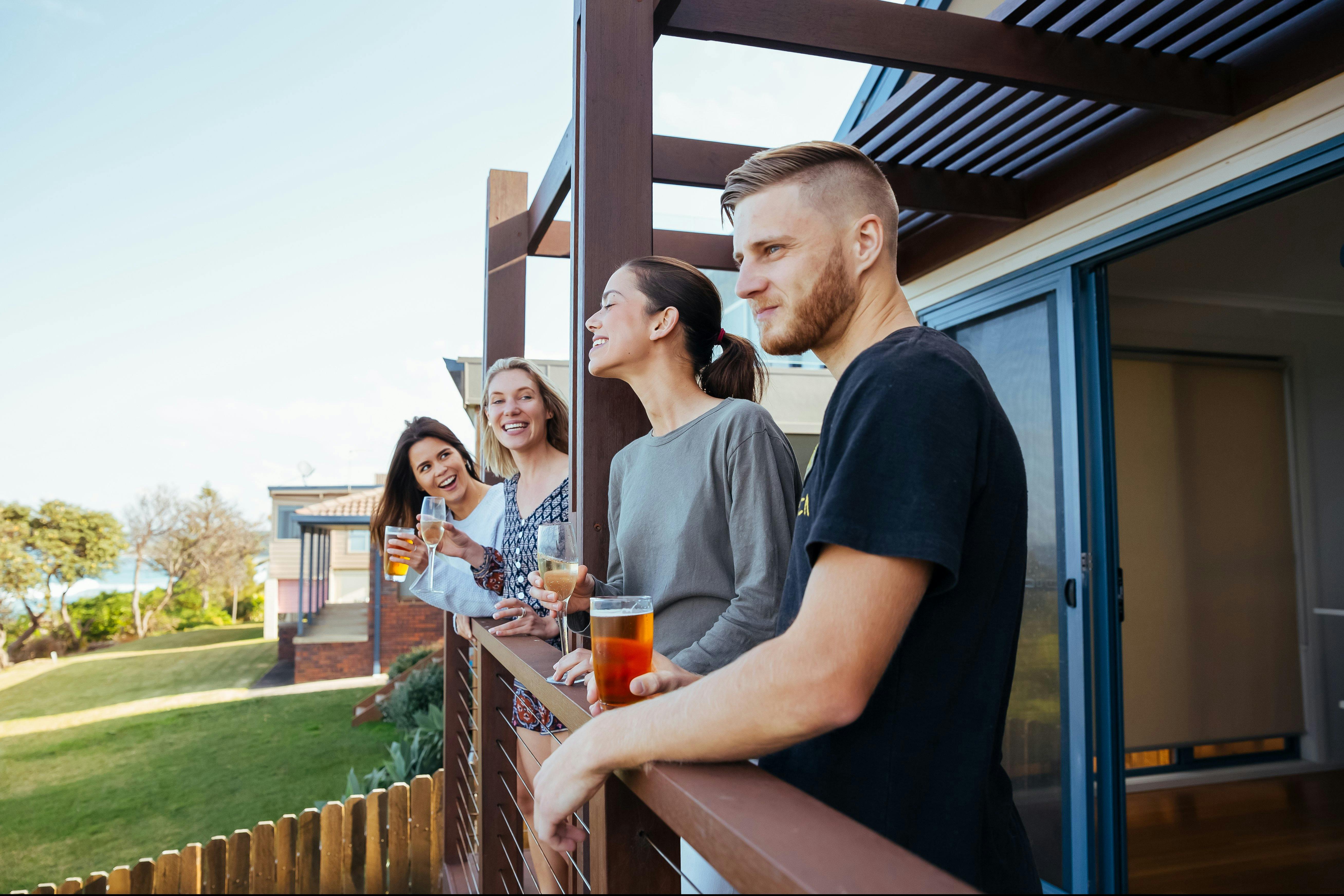 Three women and a man enjoying a drink and a laugh on the deck