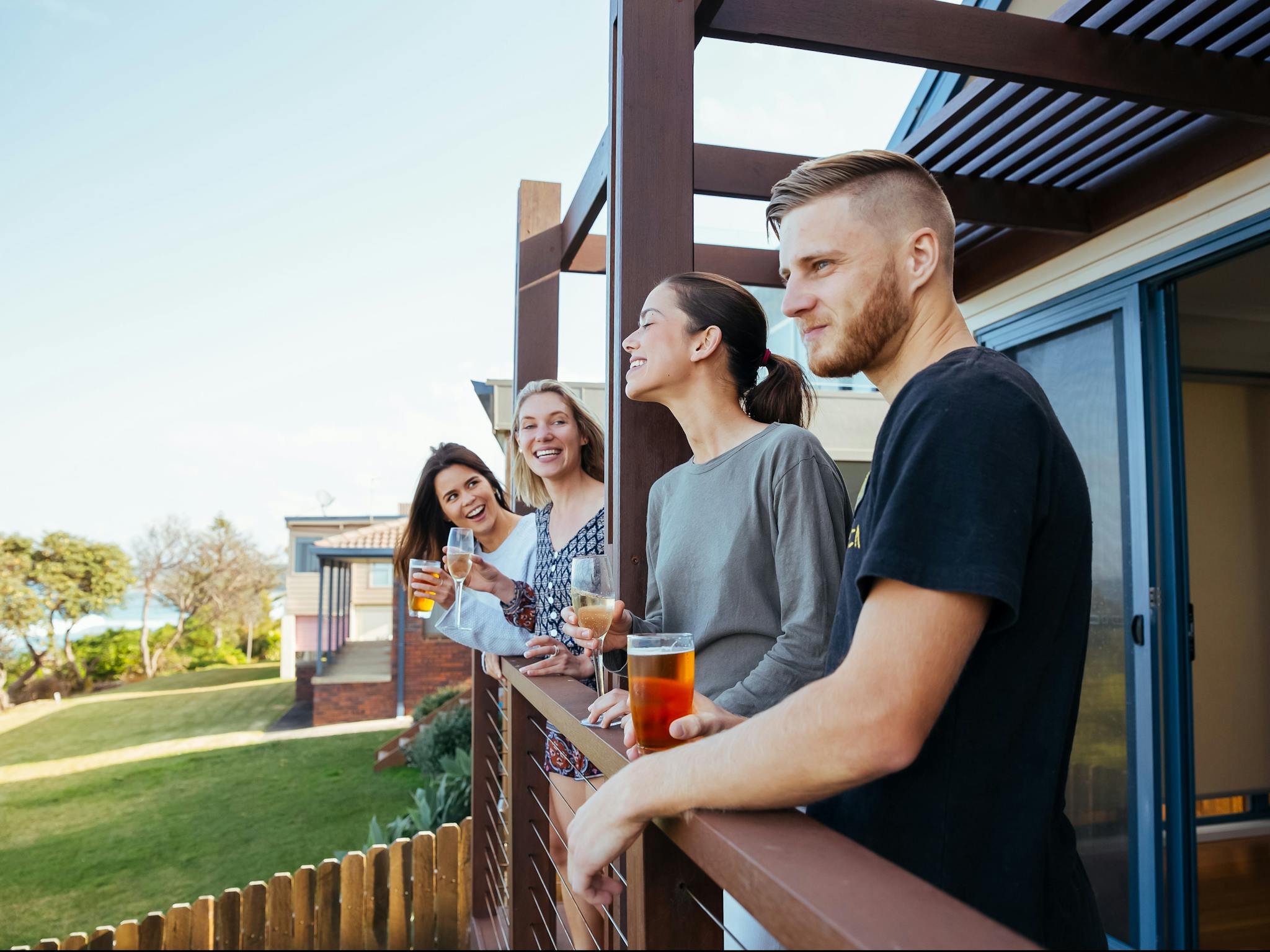 Three women and a man enjoying a drink and a laugh on the deck