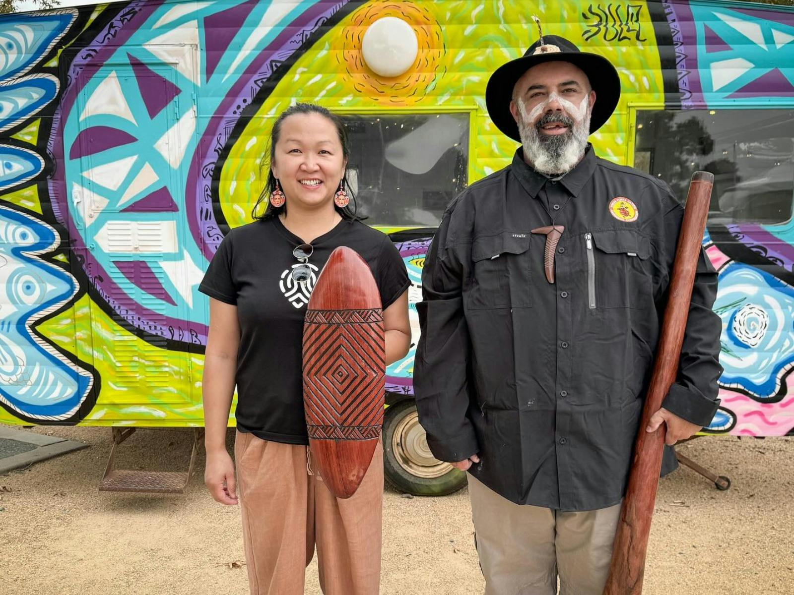 Two people standing in front of a colourful mural smiling