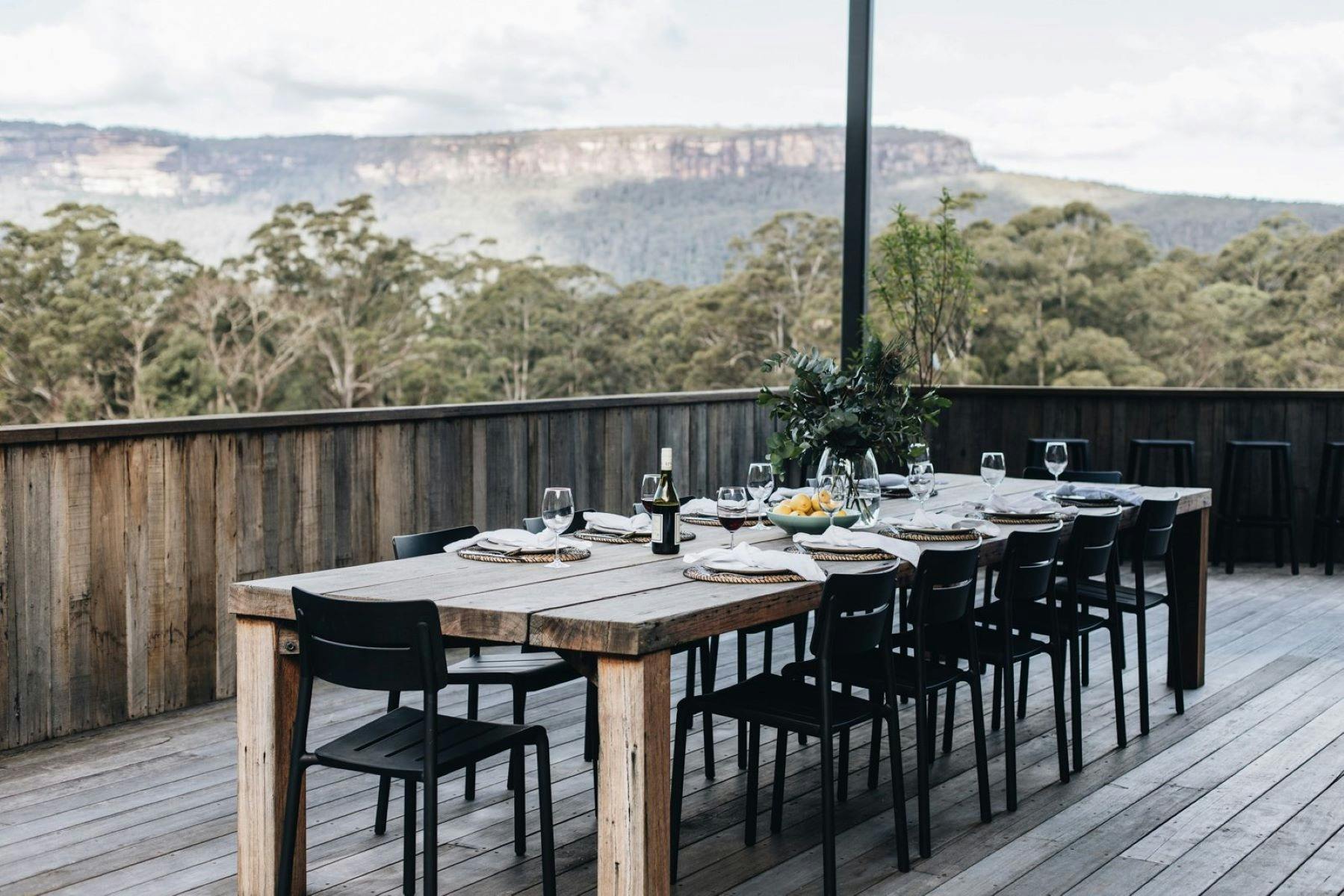 Image of outdoor dining table set for a lunch on the back deck. Mountains can be seen in the back.