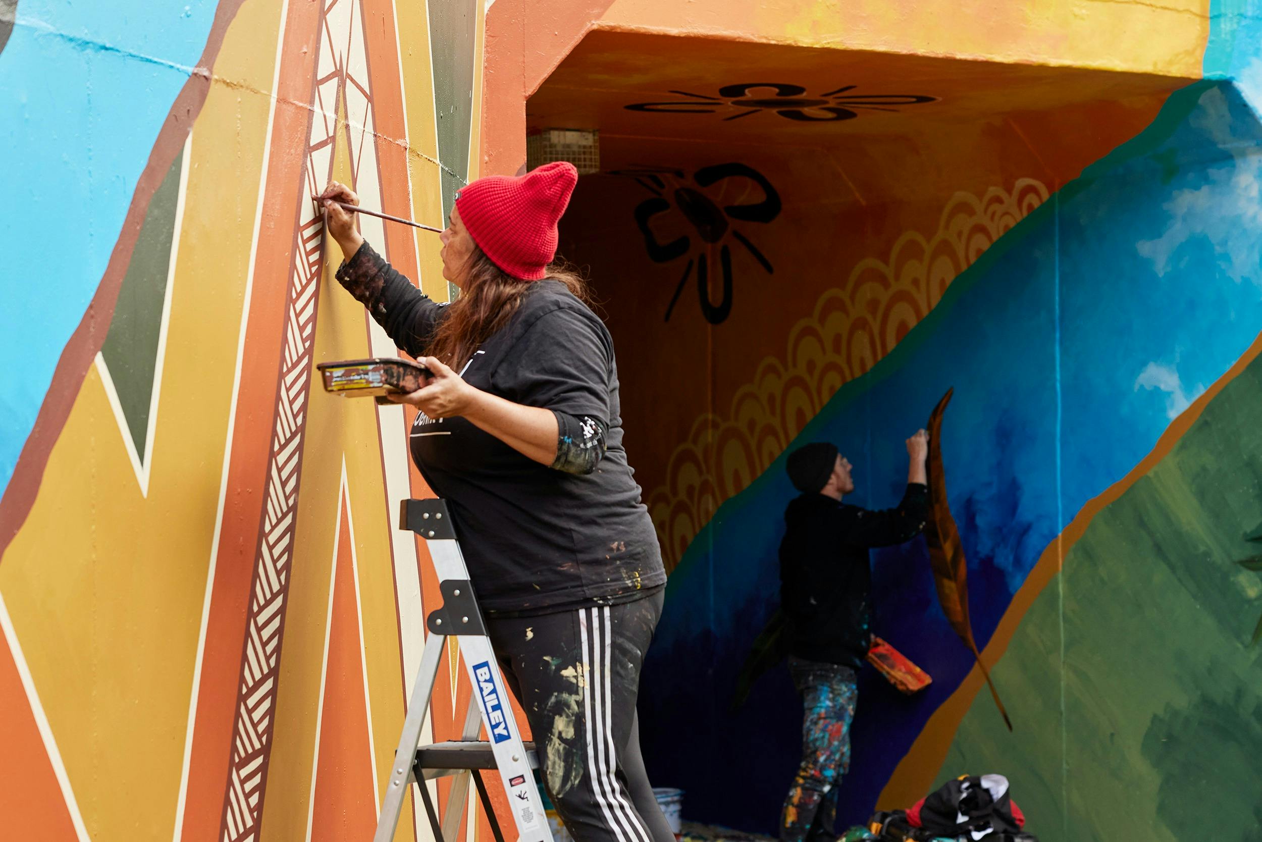 Artists Alice Pepper and MEGGS painting colourful murals on walls using blue, yellow, green, orange