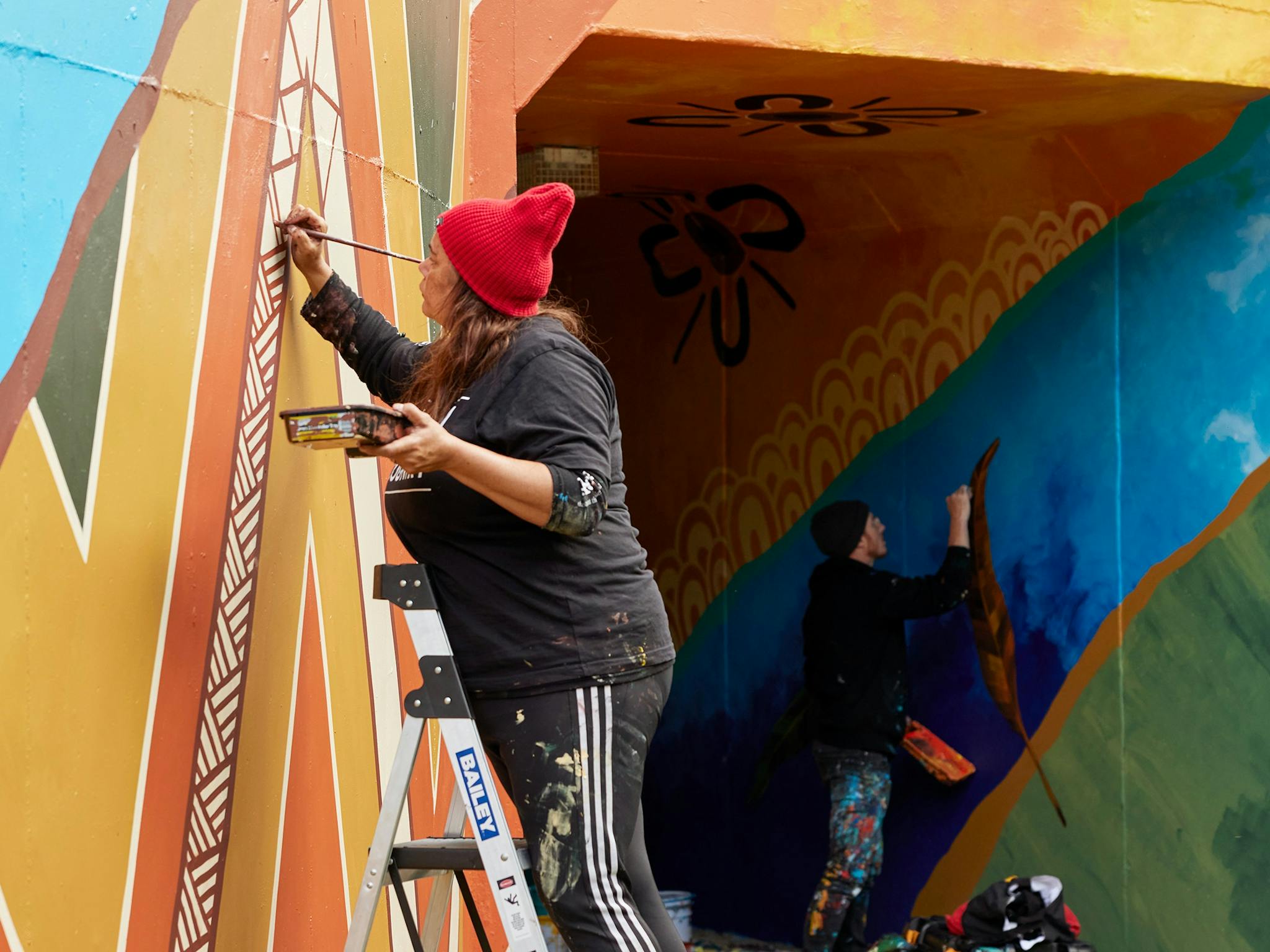 Artists Alice Pepper and MEGGS painting colourful murals on walls using blue, yellow, green, orange