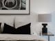 Bedroom with bed, pillows and cushions, tableside lamp and painting hanging on the wall