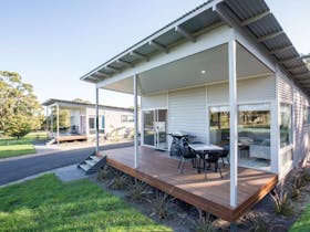 Exterior of a villa with a wooden deck, table and chairs and steps leading down to grass