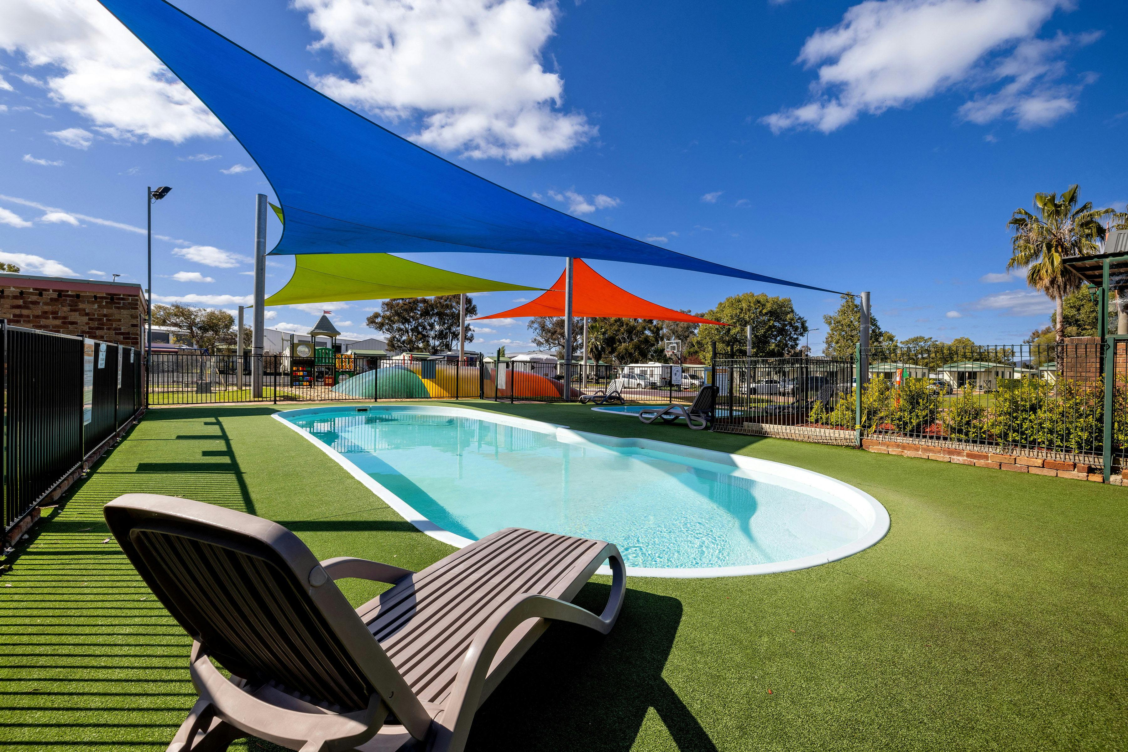 Image of lovely oval pool, surrounded by grass, shade sails  and a lilo.