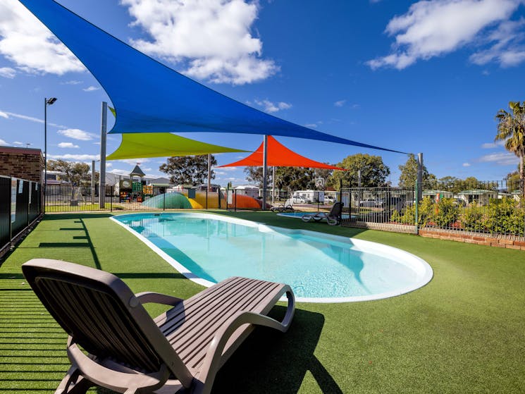 Image of lovely oval pool, surrounded by grass, shade sails  and a lilo.