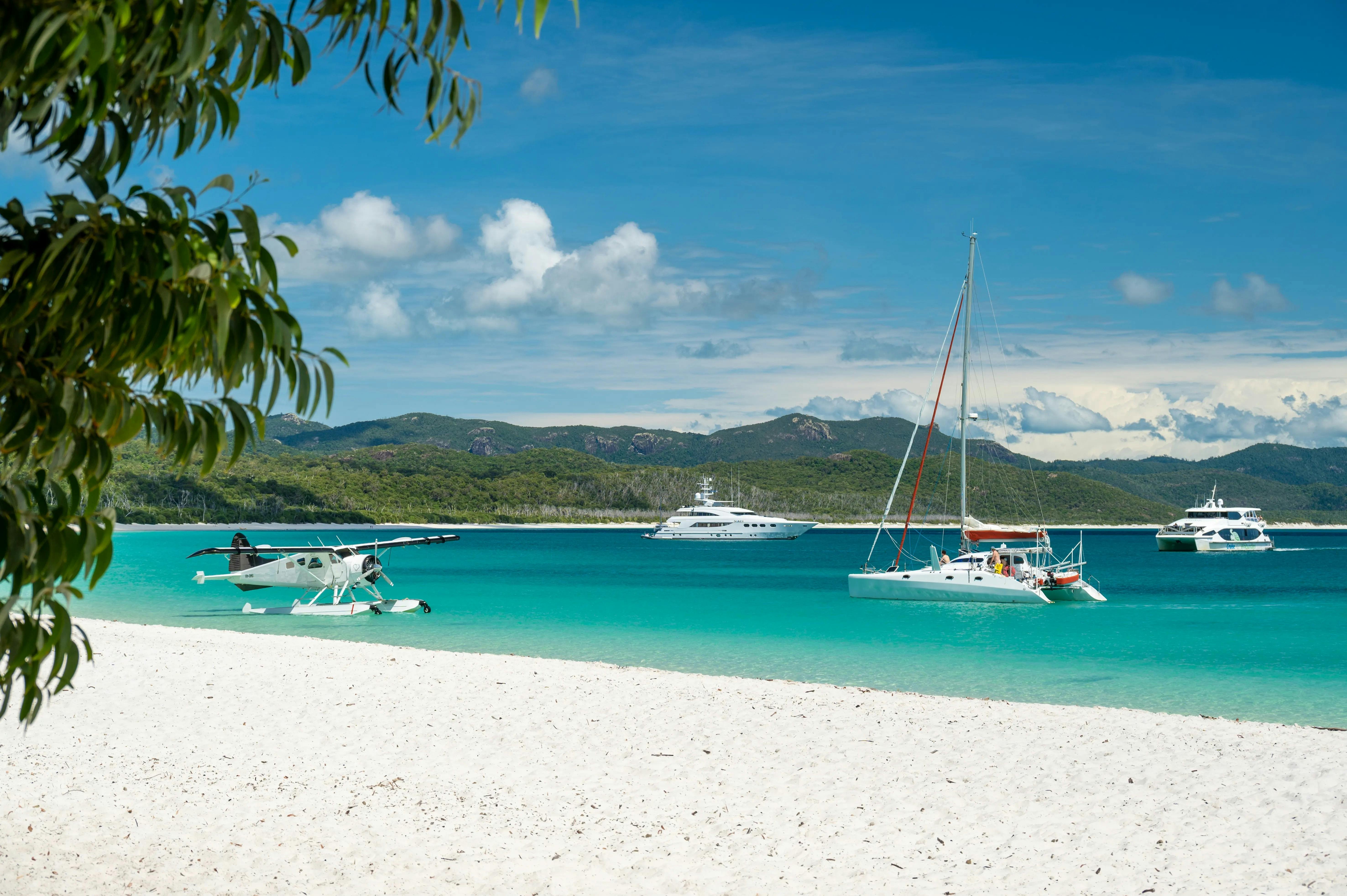 Seaplane and sailing boats anchored along the white sandy beach and blue waters