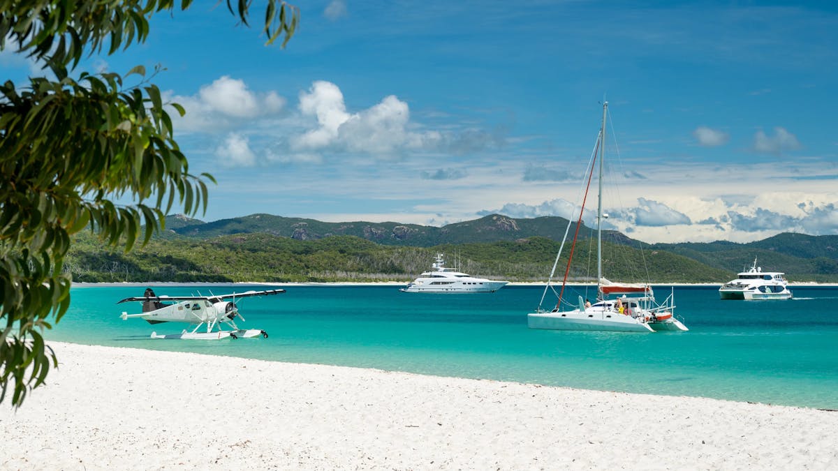 Seaplane and sailing boats anchored along the white sandy beach and blue waters