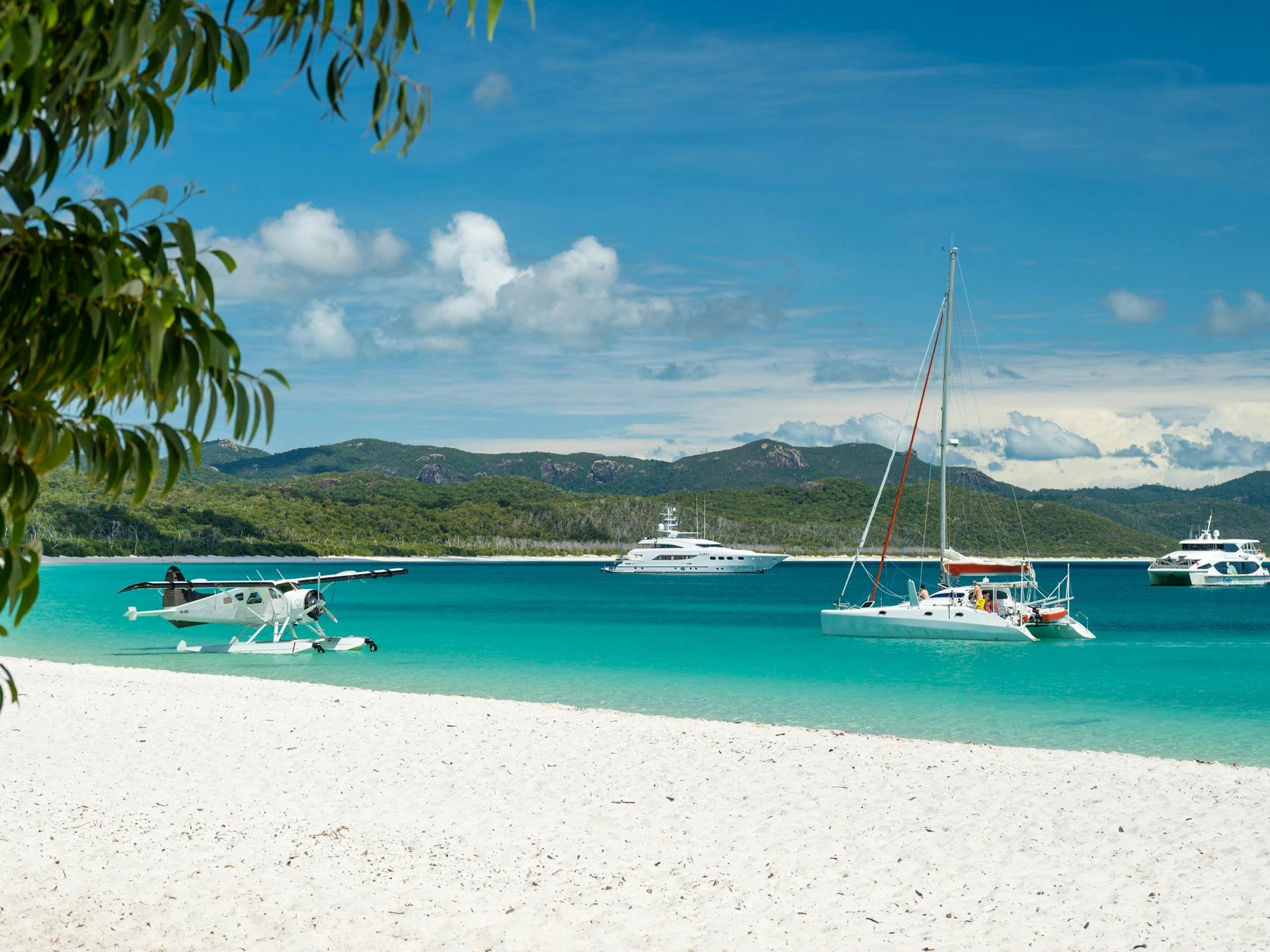 Seaplane and sailing boats anchored along the white sandy beach and blue waters