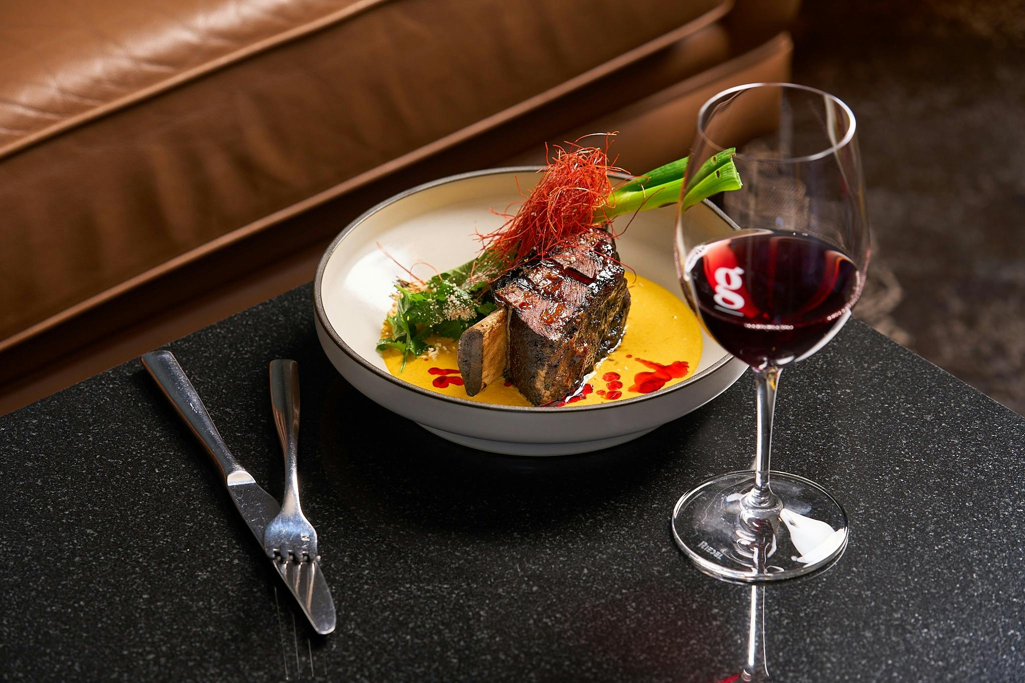Beautifully presented steak, glass of red wine in lounge with brown leather chair and marble table