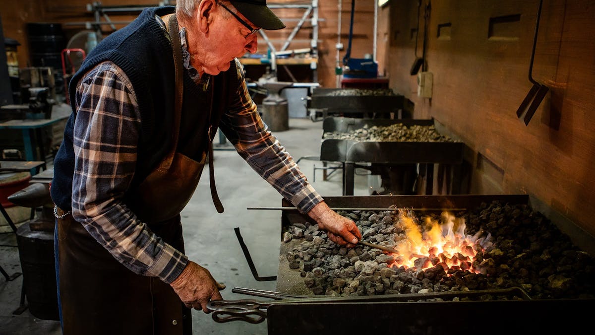 Blacksmith working coals to heat metal at Cobb+Co.