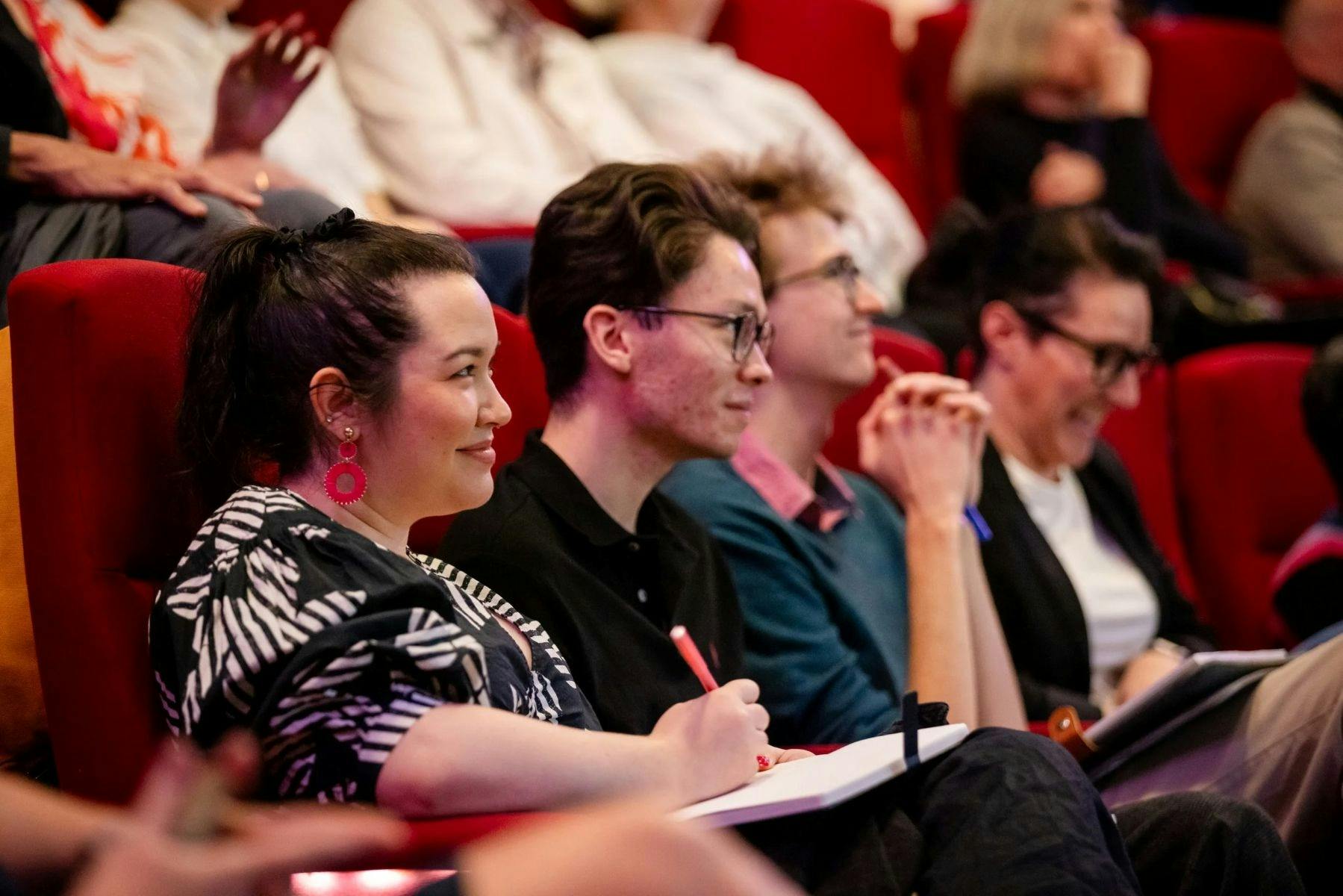 People sitting in a theatre smiling and listening to the speakers