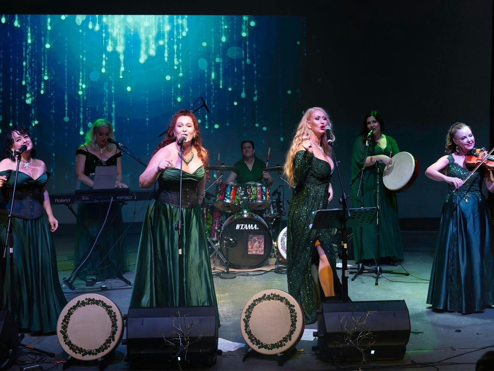 Women on a stage in green dresses playing traditional Irish instruments and singing