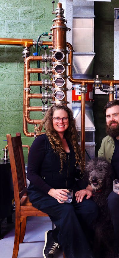 Renee & David, distillery founders, sitting in front of their still with their dog Parker.