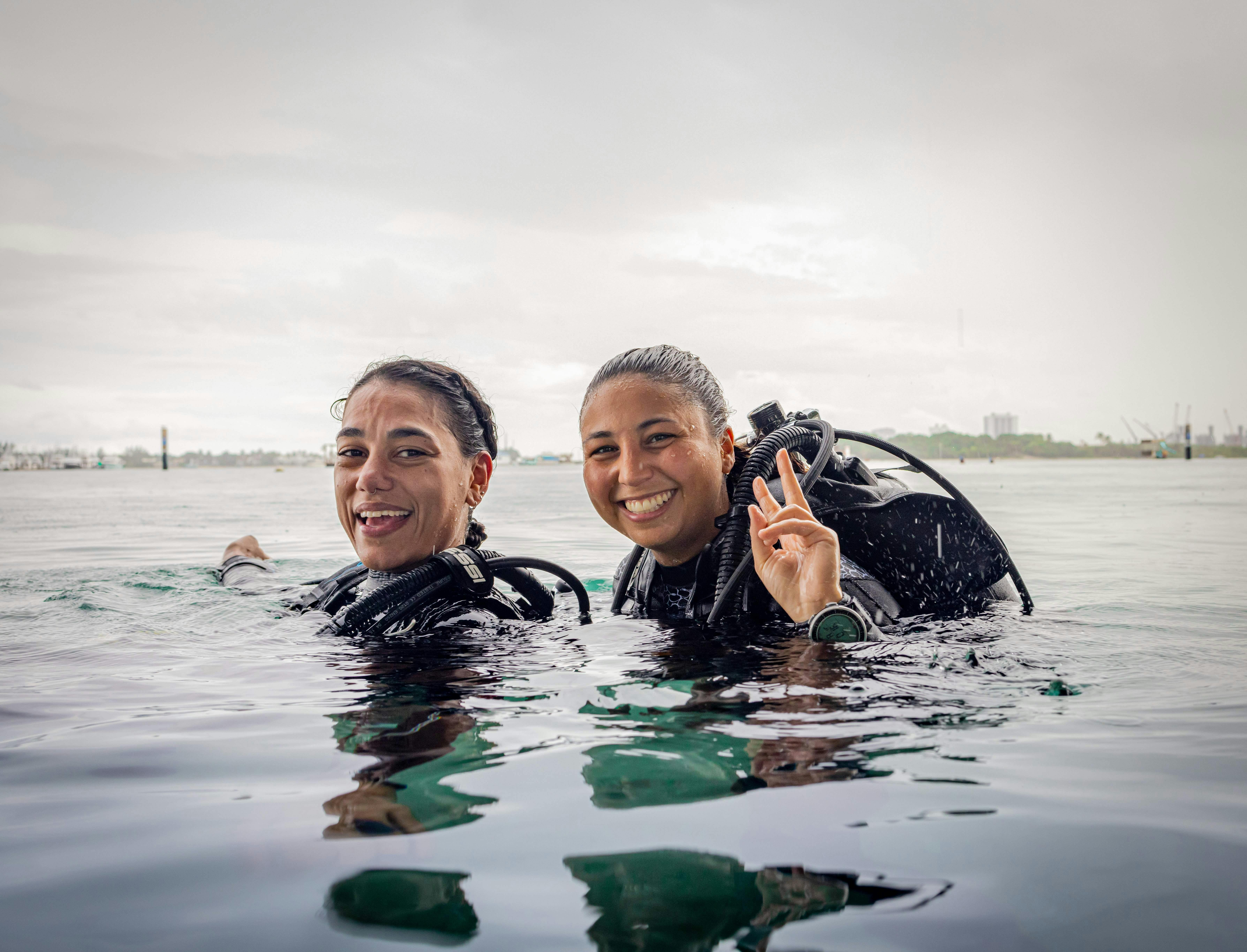 Two smiling scuba divers floating at the surface after a dive, wearing scuba equipment.