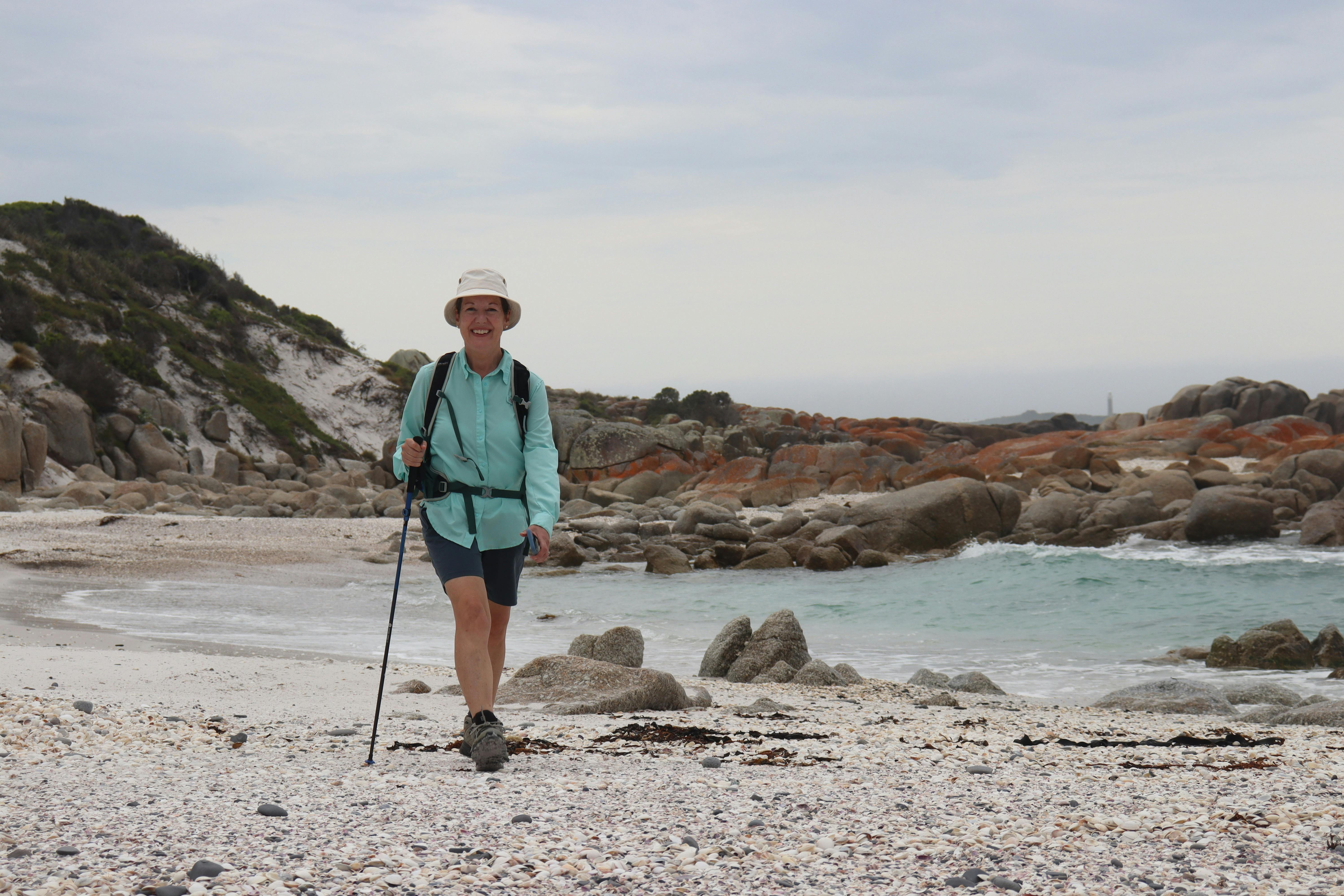 Woman walking on a beach with hiking poles during a Bay of Fires pack free walking tour in Tasmania.