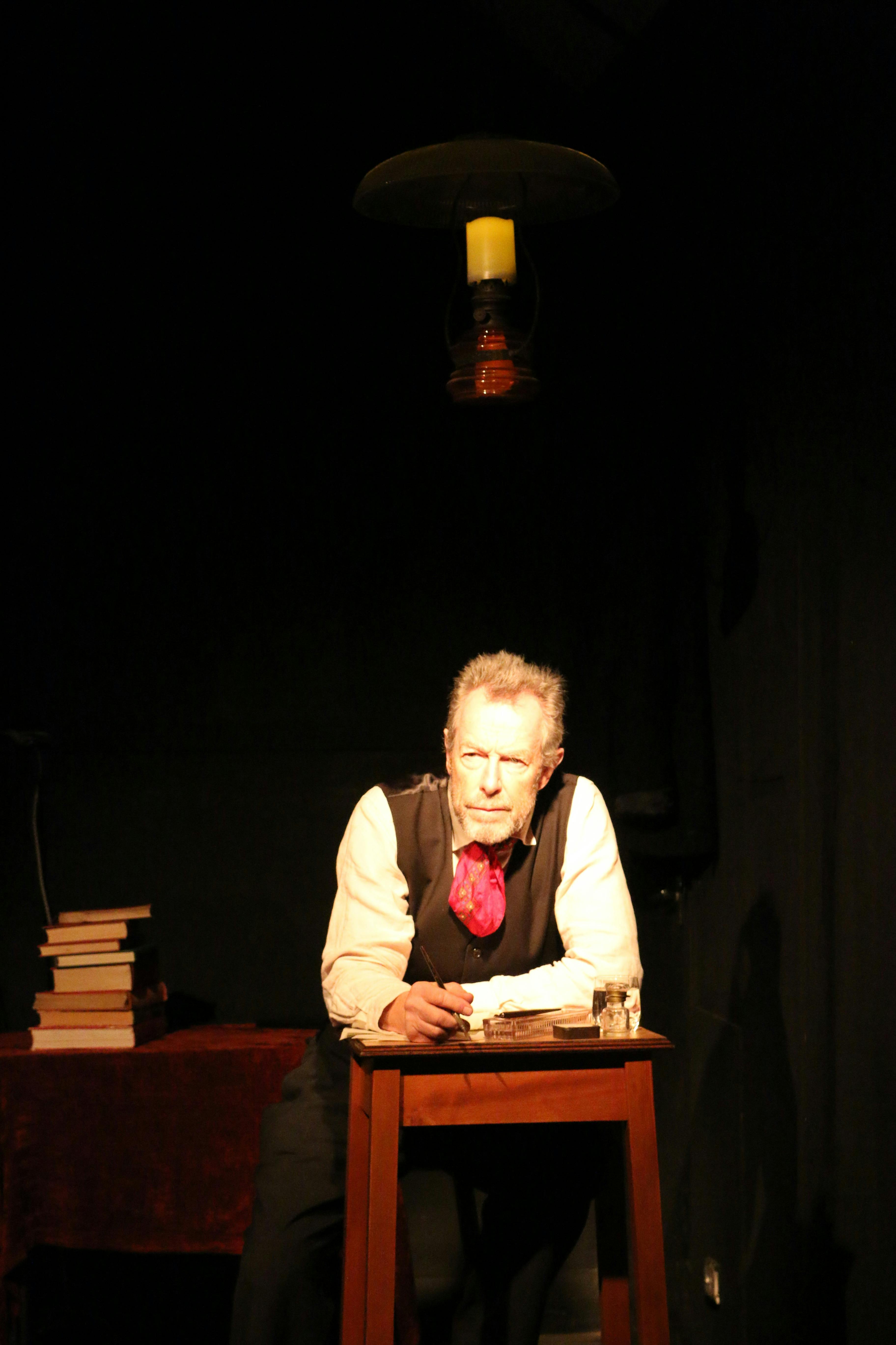 Actor Patrick Dickson sits at a desk with books as he plays the role of Victor Hugo