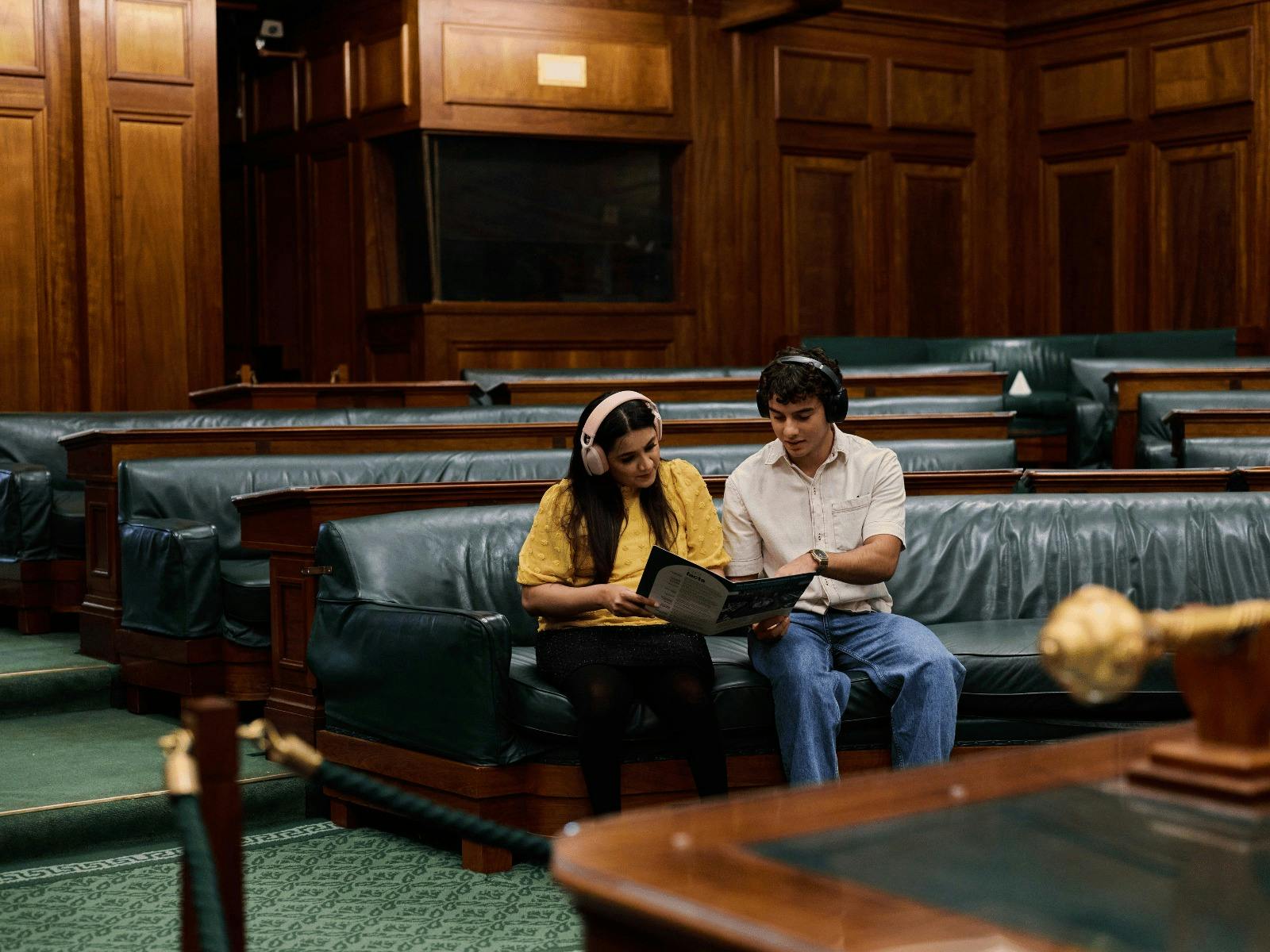 Two people seated in the House of Representatives listening to an audio guide