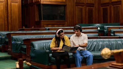 Two people seated in the House of Representatives listening to an audio guide