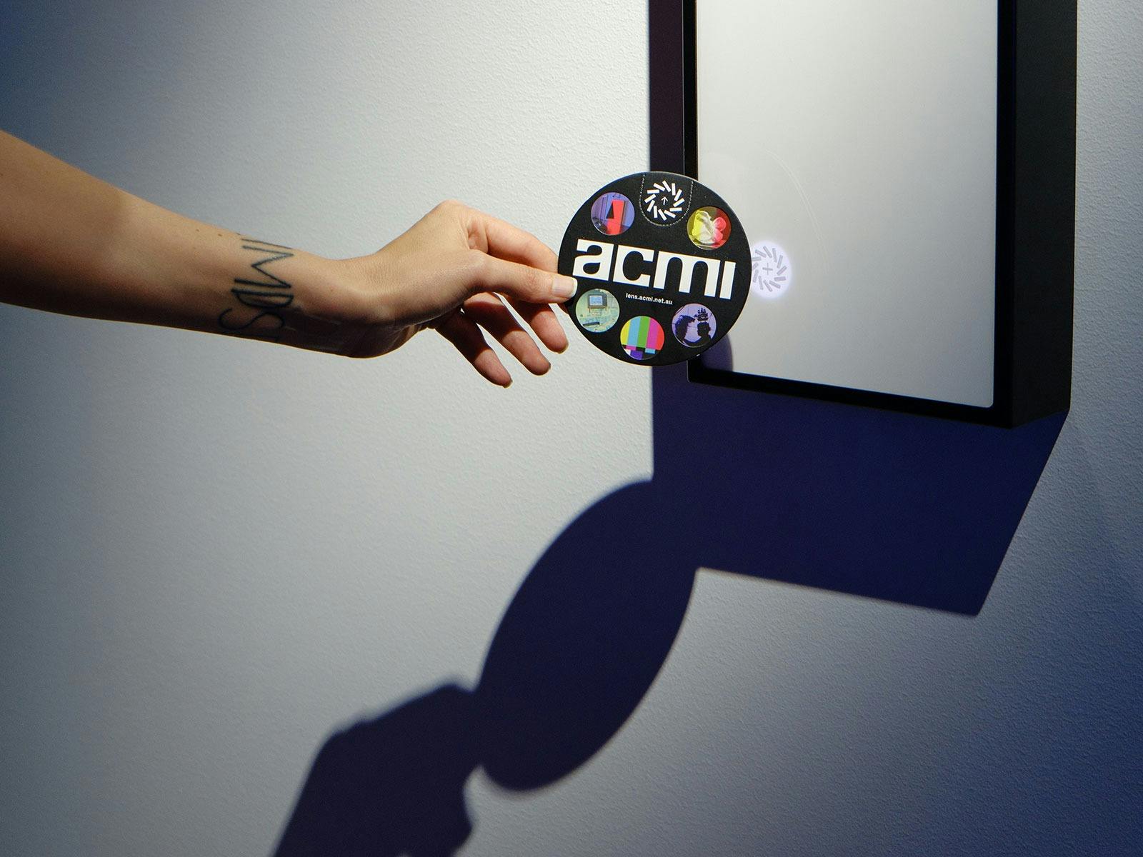 A hand holds a circular disc up to a white box