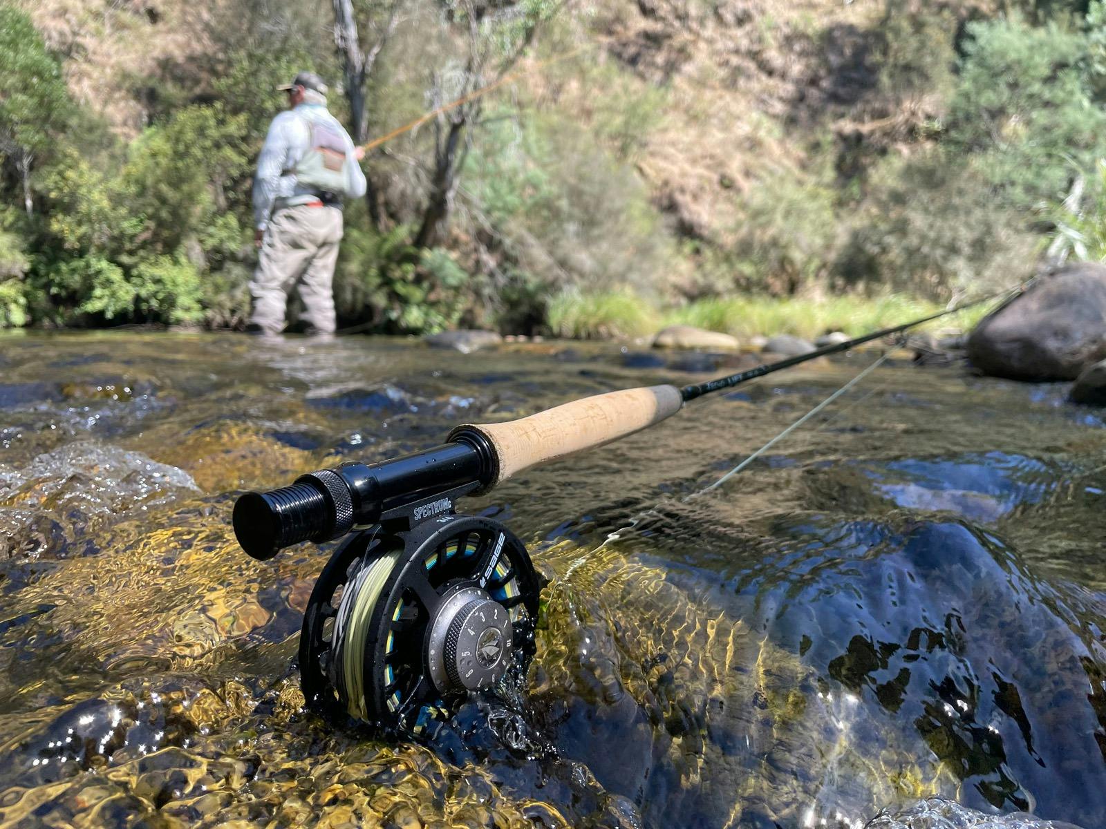 Fly fishing rod resting on a rock in a stream, with a man fishing in the background