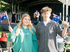 Two young people stand side by side waving Australian flags