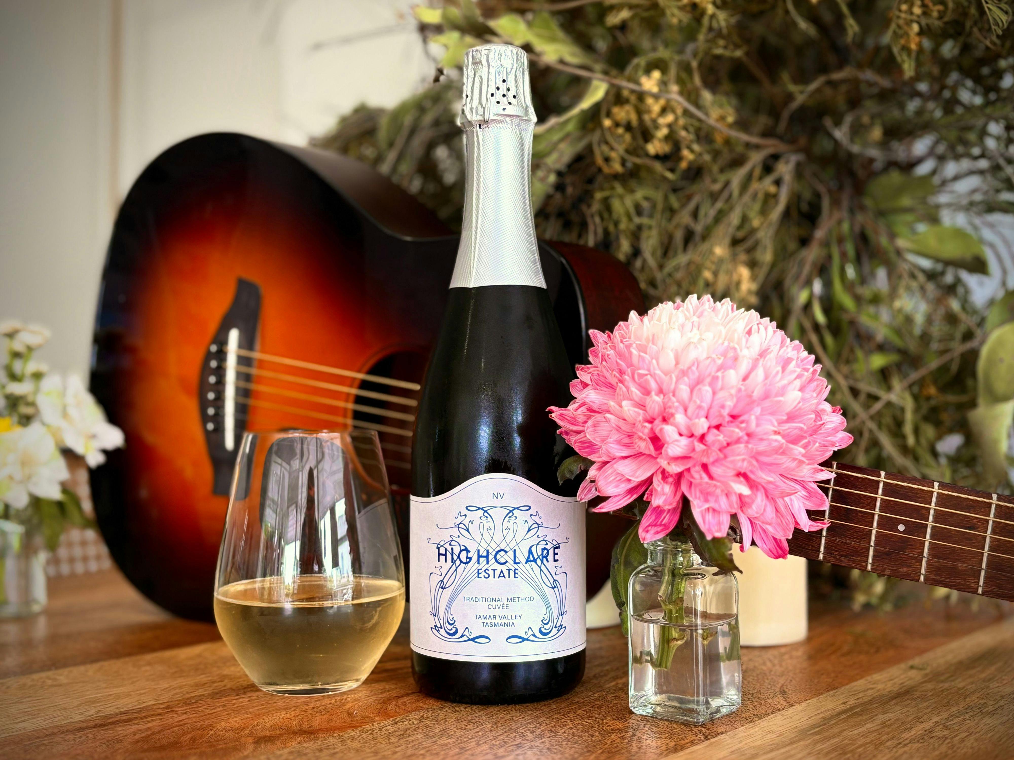 Bottle of wine, glass of wine, pink dahlia flower in small vase, black and brown guitar