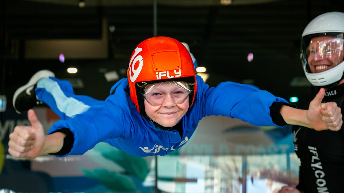 Close up of young boy with thumbs up . Smiling instructor in the background.