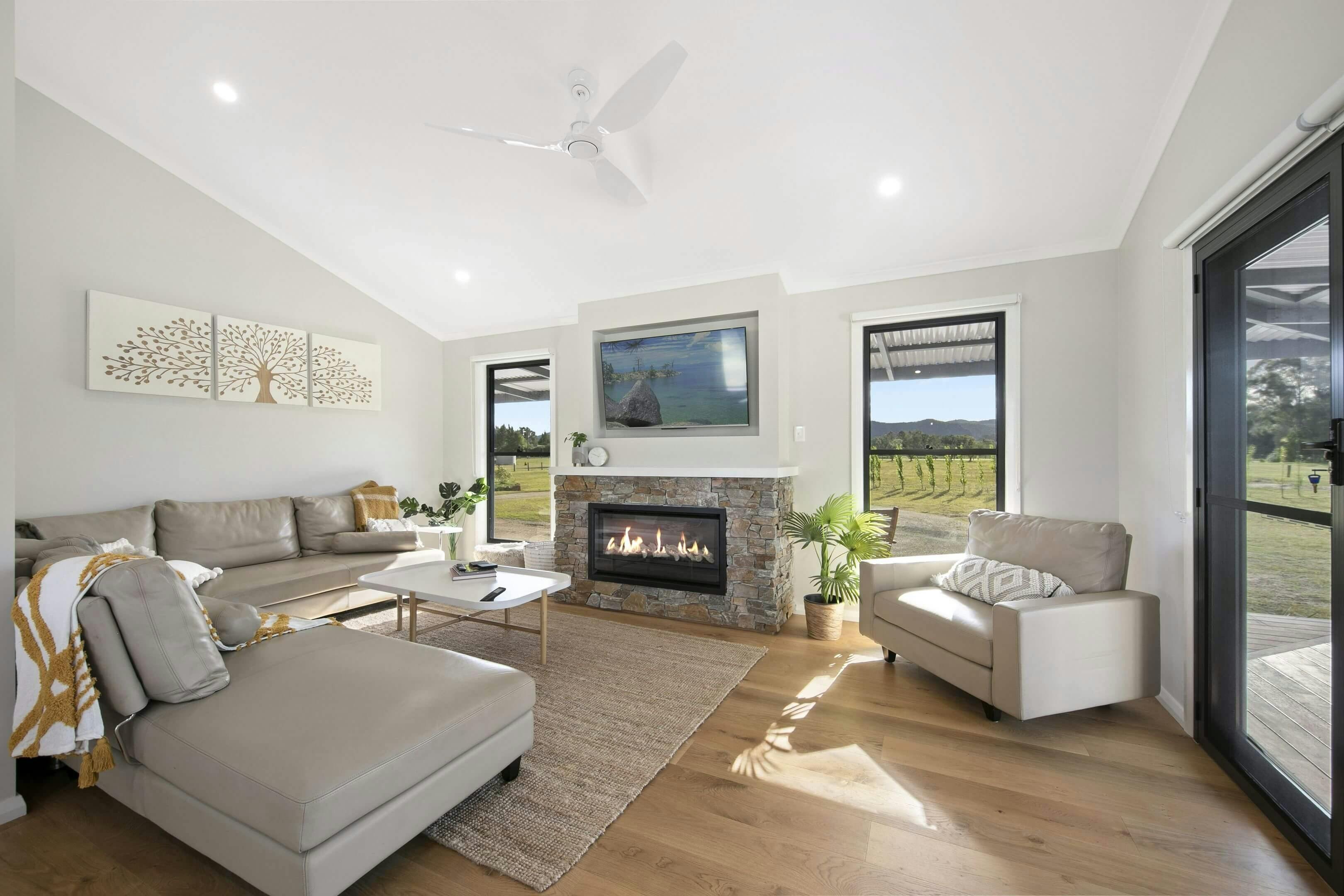 Modern living room with a stone fireplace, smart TV, wooden floors, large windows with views